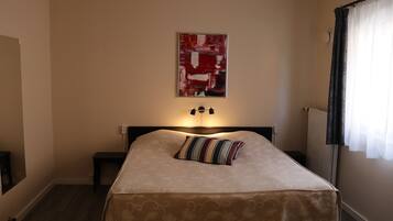 A bedroom with a bed, a nightstand, a lamp, a wall-mounted artwork, and a window with curtains.
