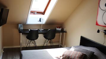 Une chambre à coucher comprenant un lit, un bureau, deux chaises, un puits de lumière et un téléviseur fixé au mur.