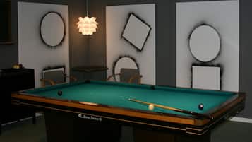 A pool table with a cue stick, surrounded by chairs and a small table.
