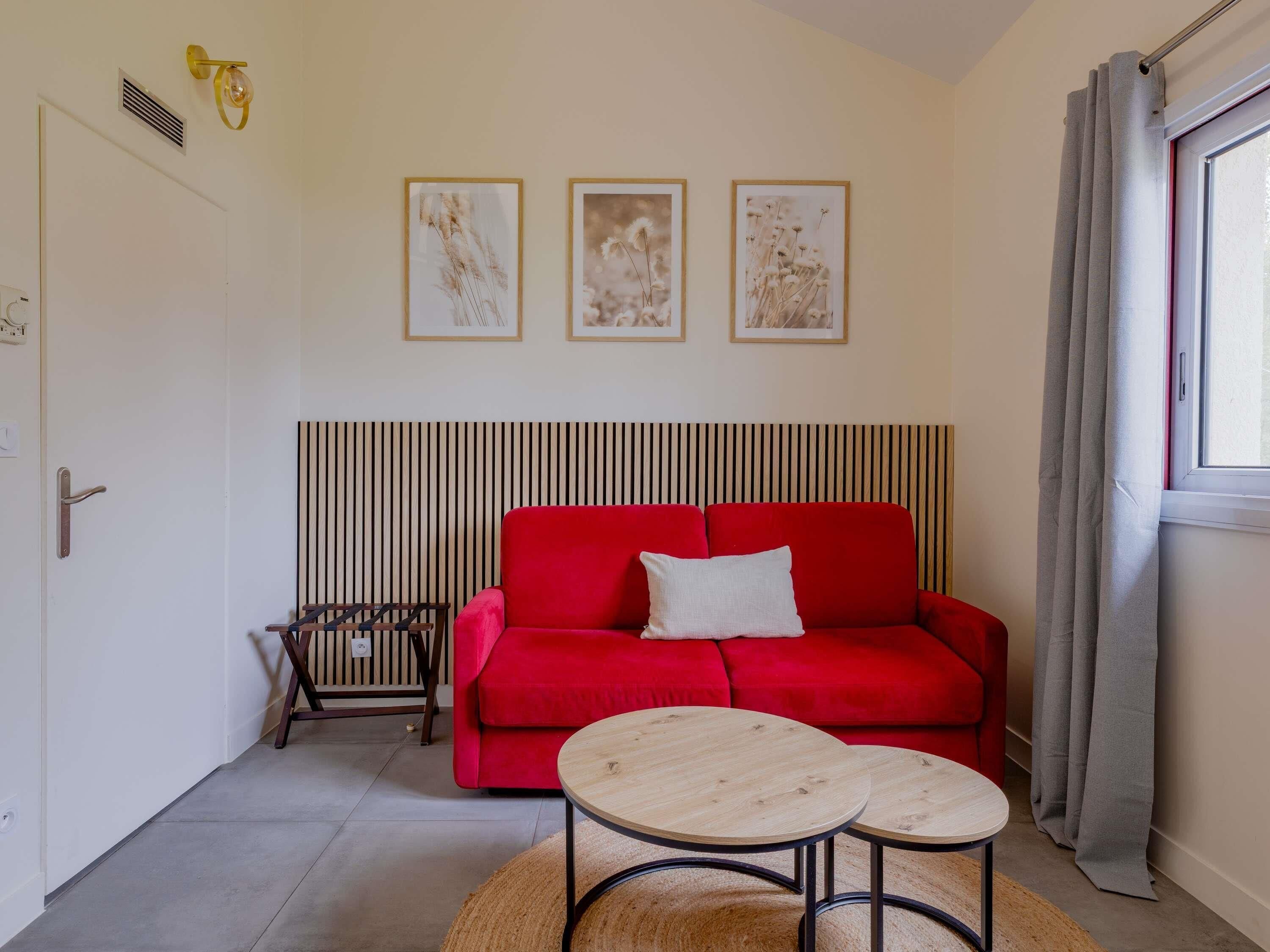 Ein rotes Sofa, zwei runde Holztische, eine gestreifte Wand und drei gerahmte Bilder.