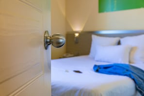 A hotel room with a bed, a bedside table, and a wall-mounted lamp. - Mercure Lyon Est Villefontaine (Vaulx-Milieu)