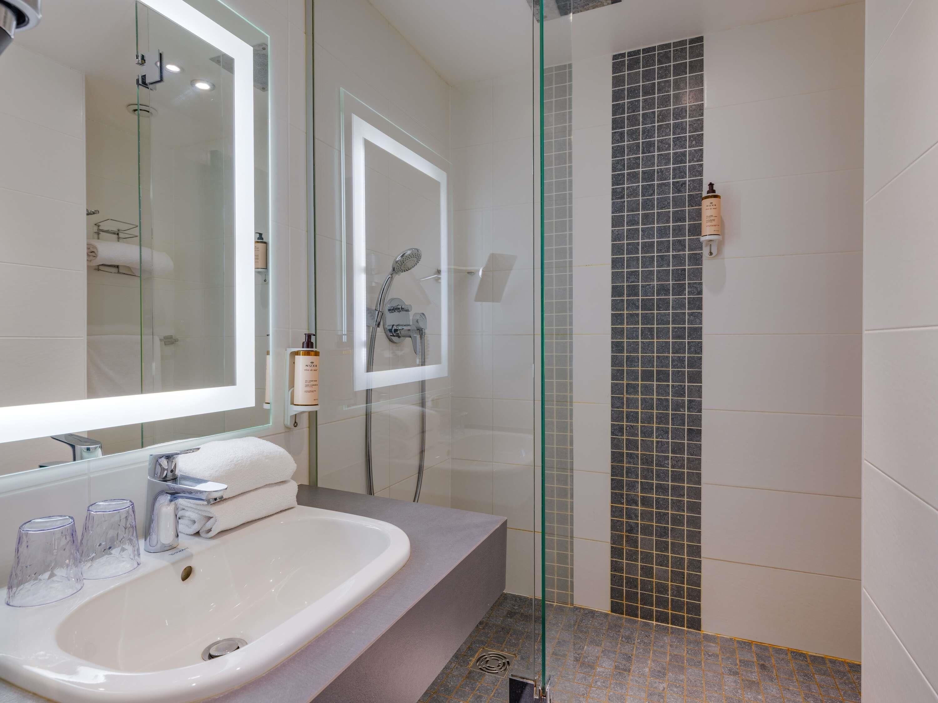 A modern bathroom with a glass-enclosed shower, a white sink, and a mirror.
