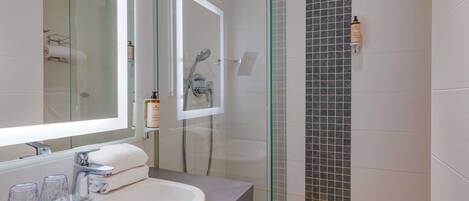 Un baño moderno con ducha de vidrio, un lavamanos blanco y un espejo.