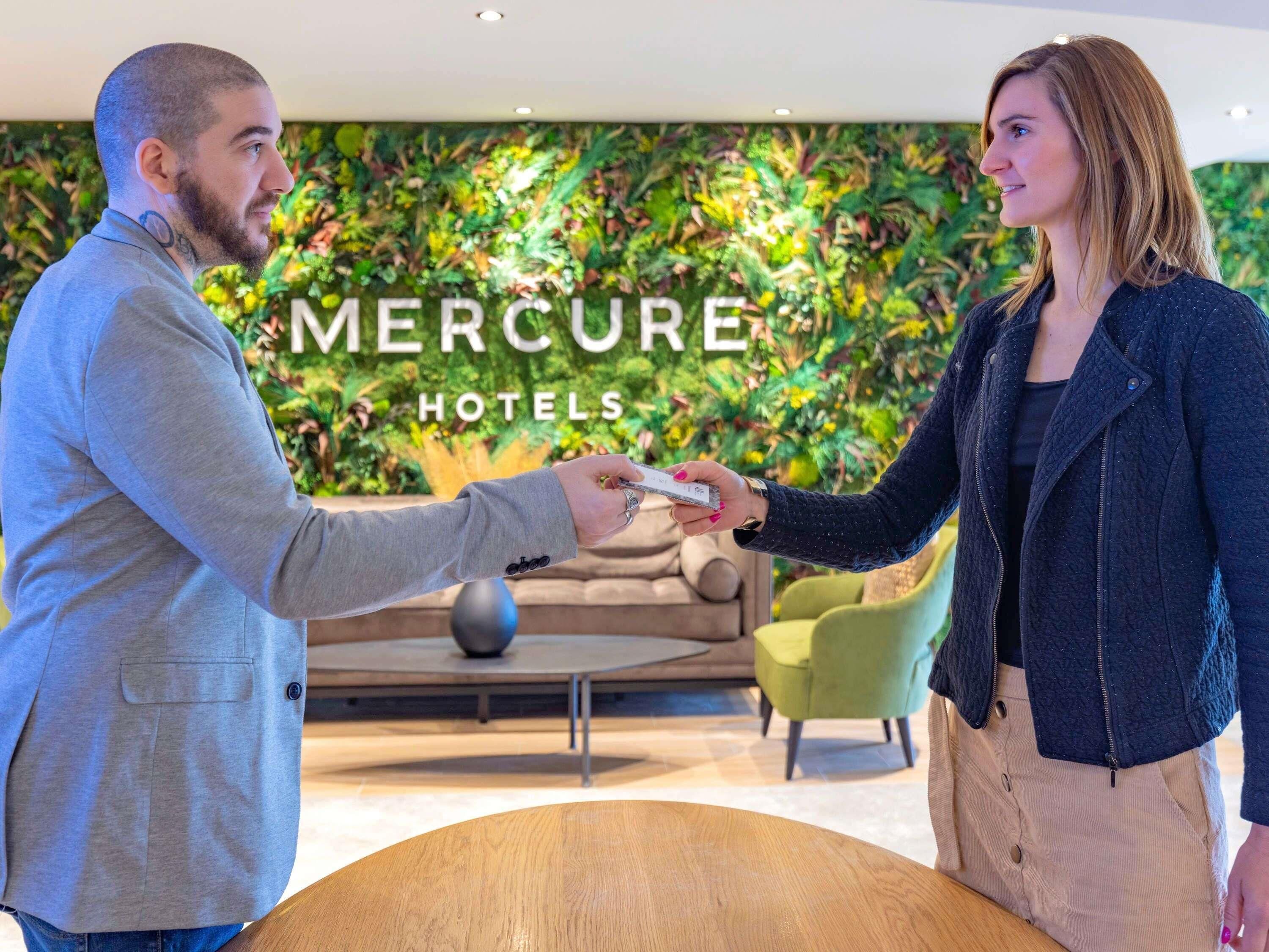 Dos personas intercambiando una tarjeta frente a una pared con el texto 'Mercure Hotels'.