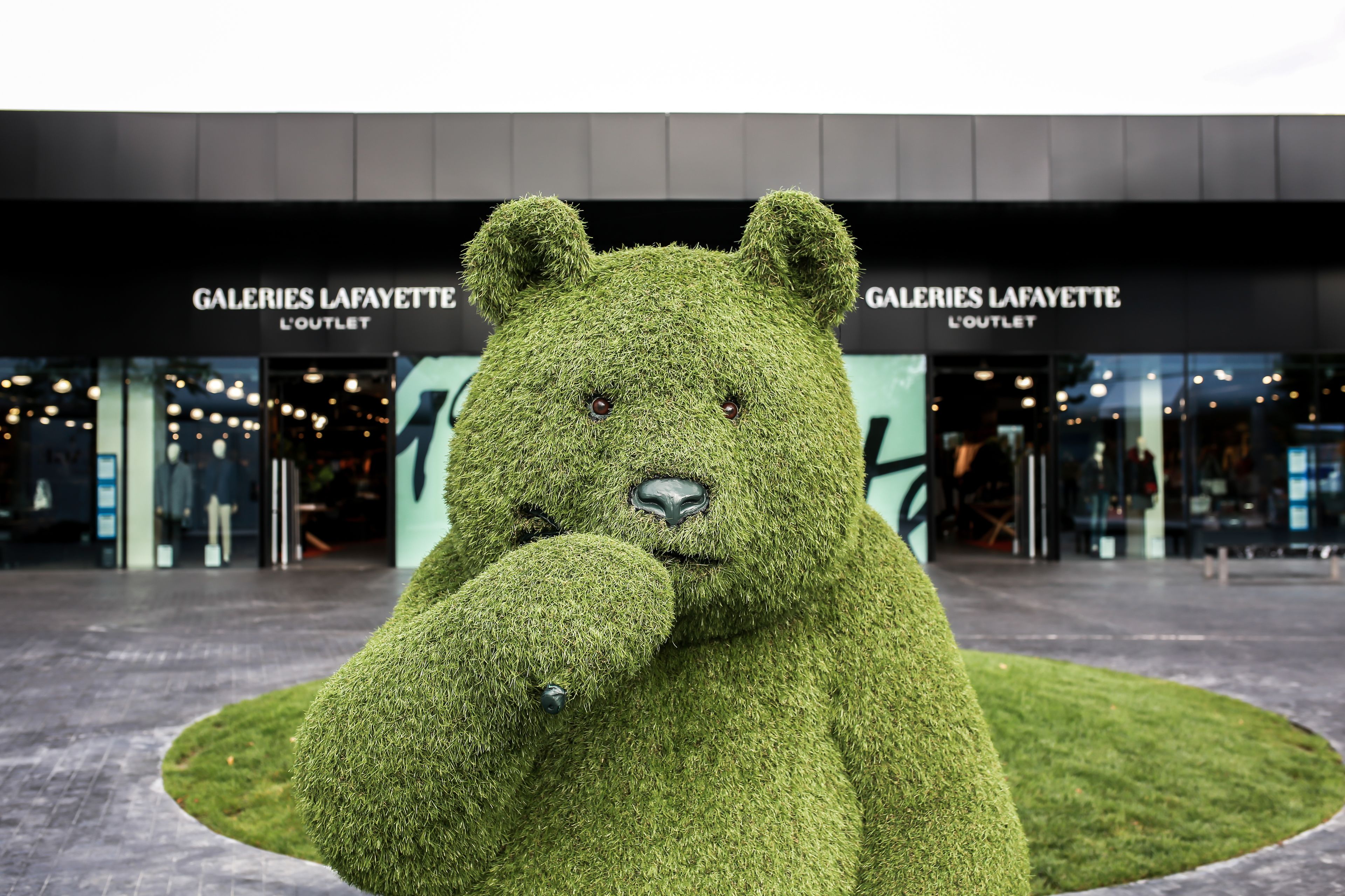 Een groot beersculptuur voor een gebouw met borden waarop staat: GALERIES LAFAYETTE L'OUTLET.