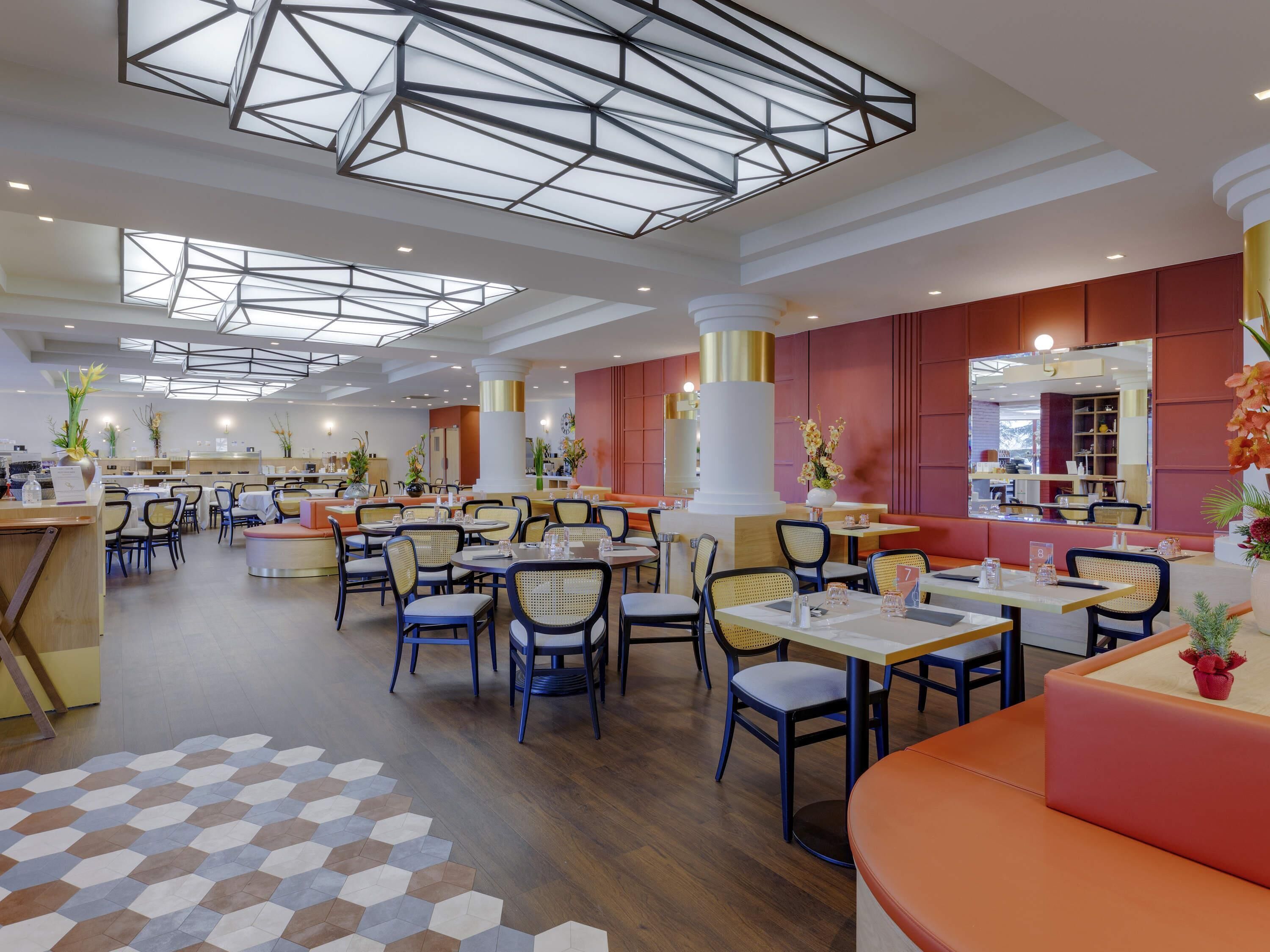A modern restaurant with high ceilings, geometric ceiling design, and a mix of seating arrangements including tables and booths.