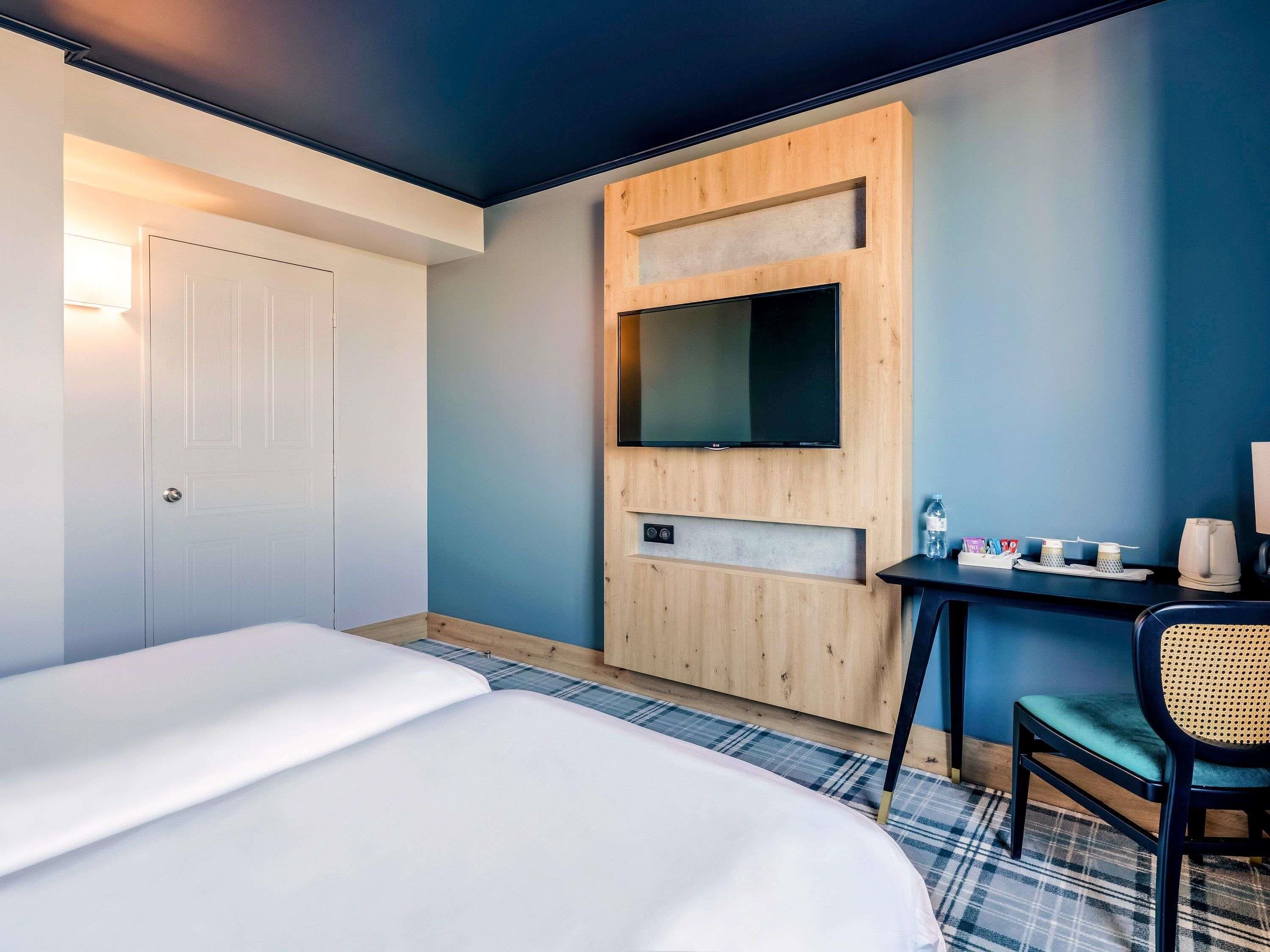 A hotel room with a bed, a desk, a chair, and a television mounted on the wall.