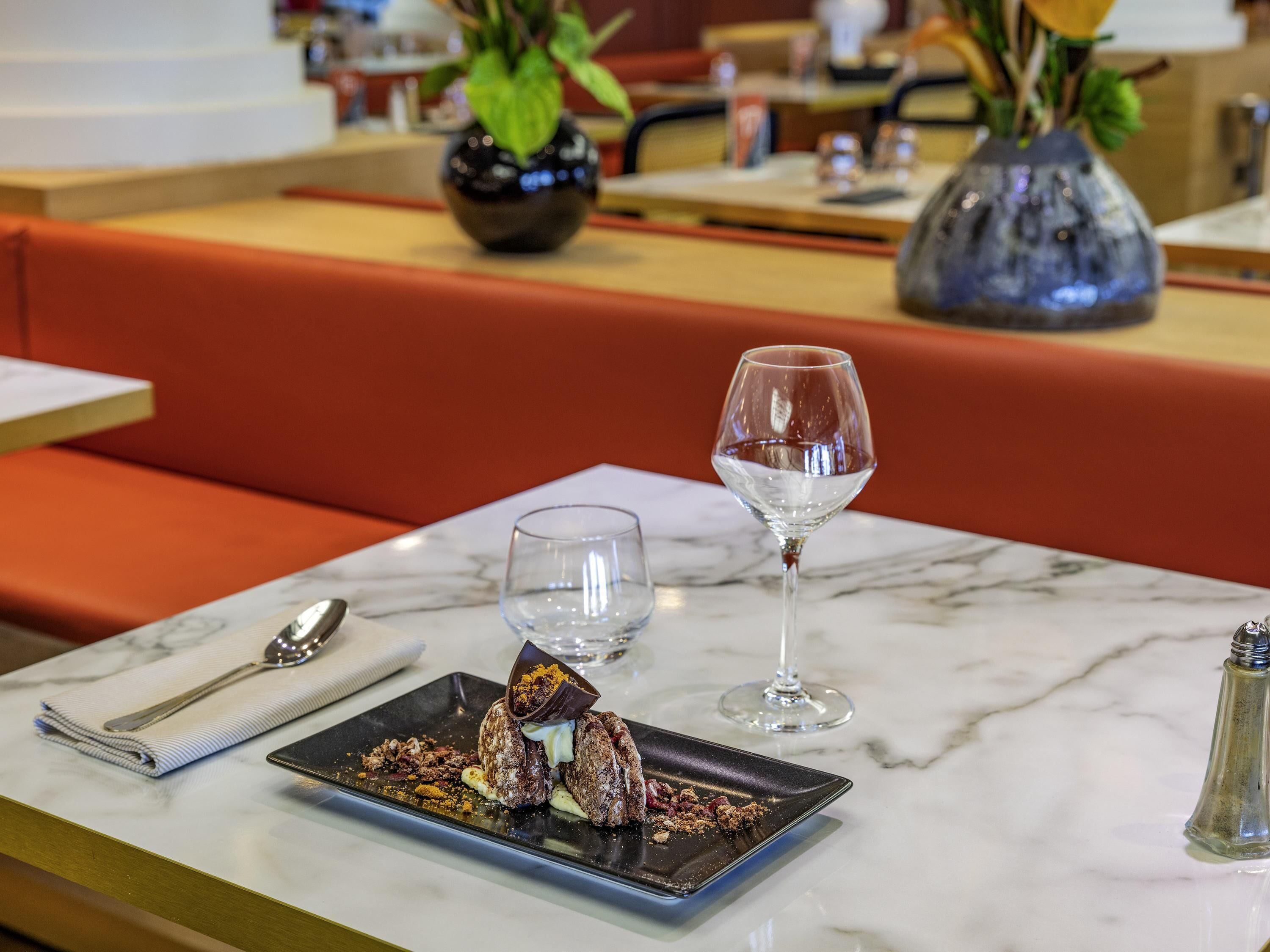 Una mesa de comedor con un plato de postre, una copa de vino y un florero con plantas.