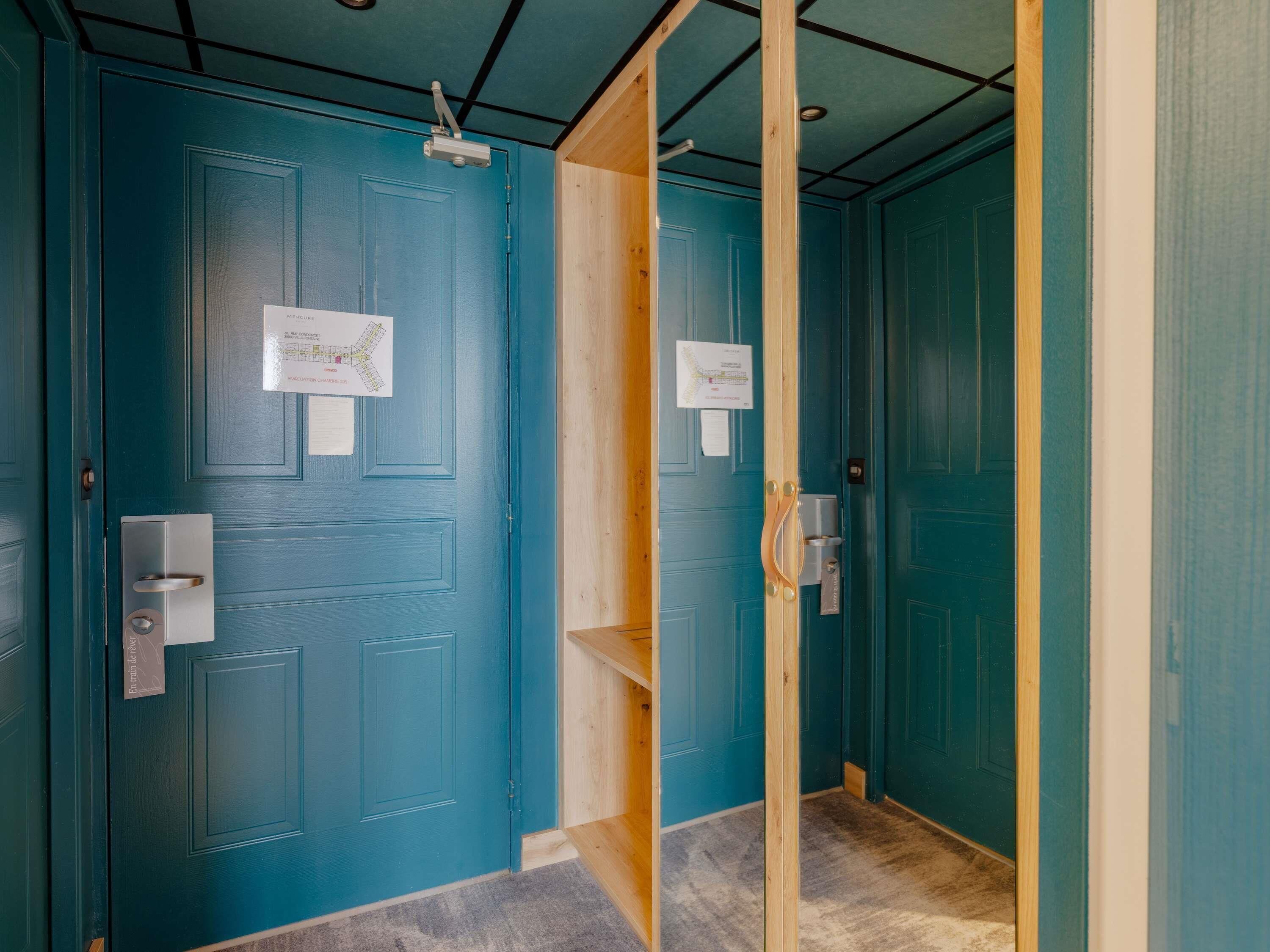 A hallway with teal doors, a wooden door frame, and a light switch on the wall.