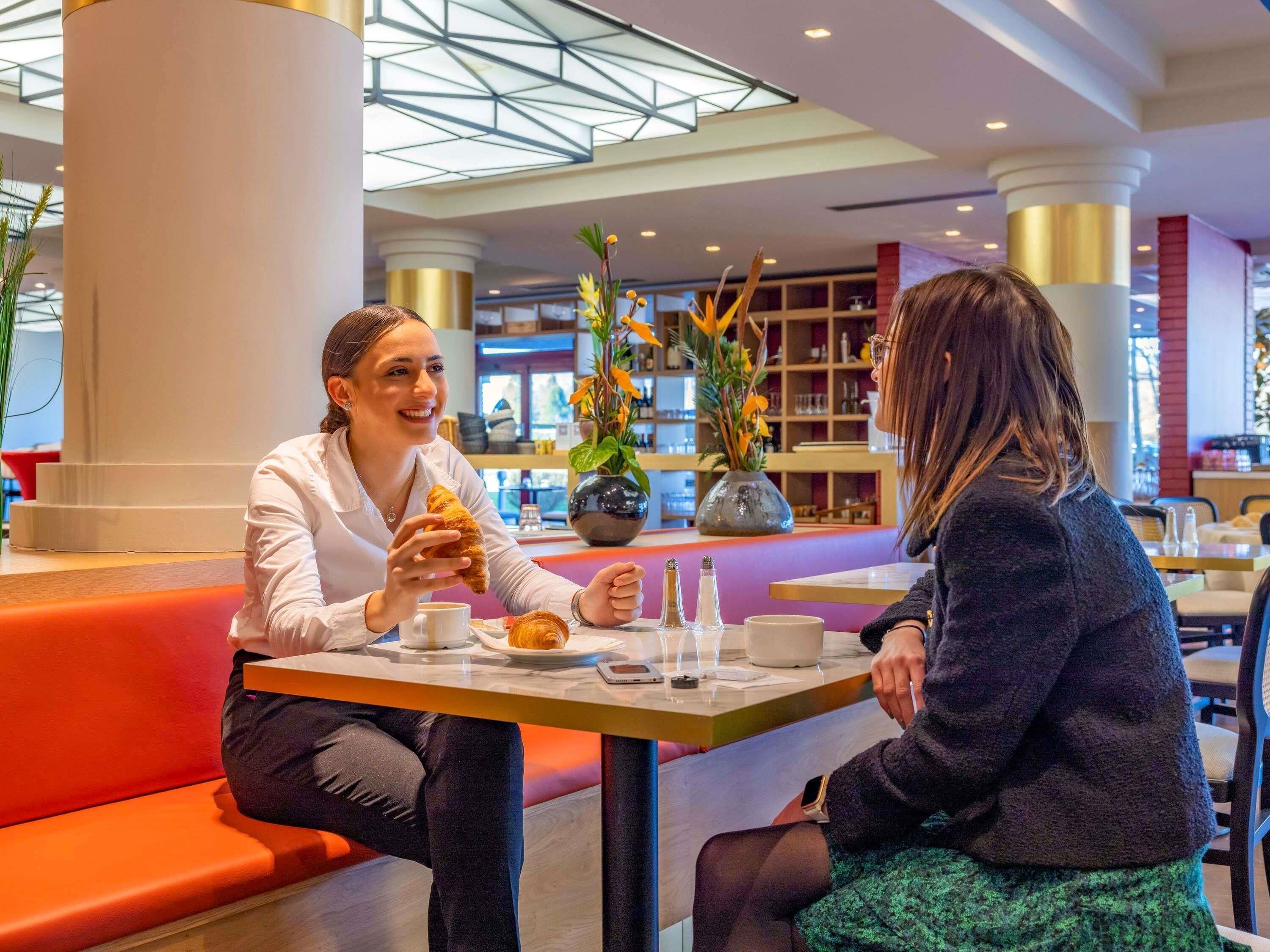 Twee personen zitten aan een tafel in een moderne ruimte met een hoge plafond en zuilen.