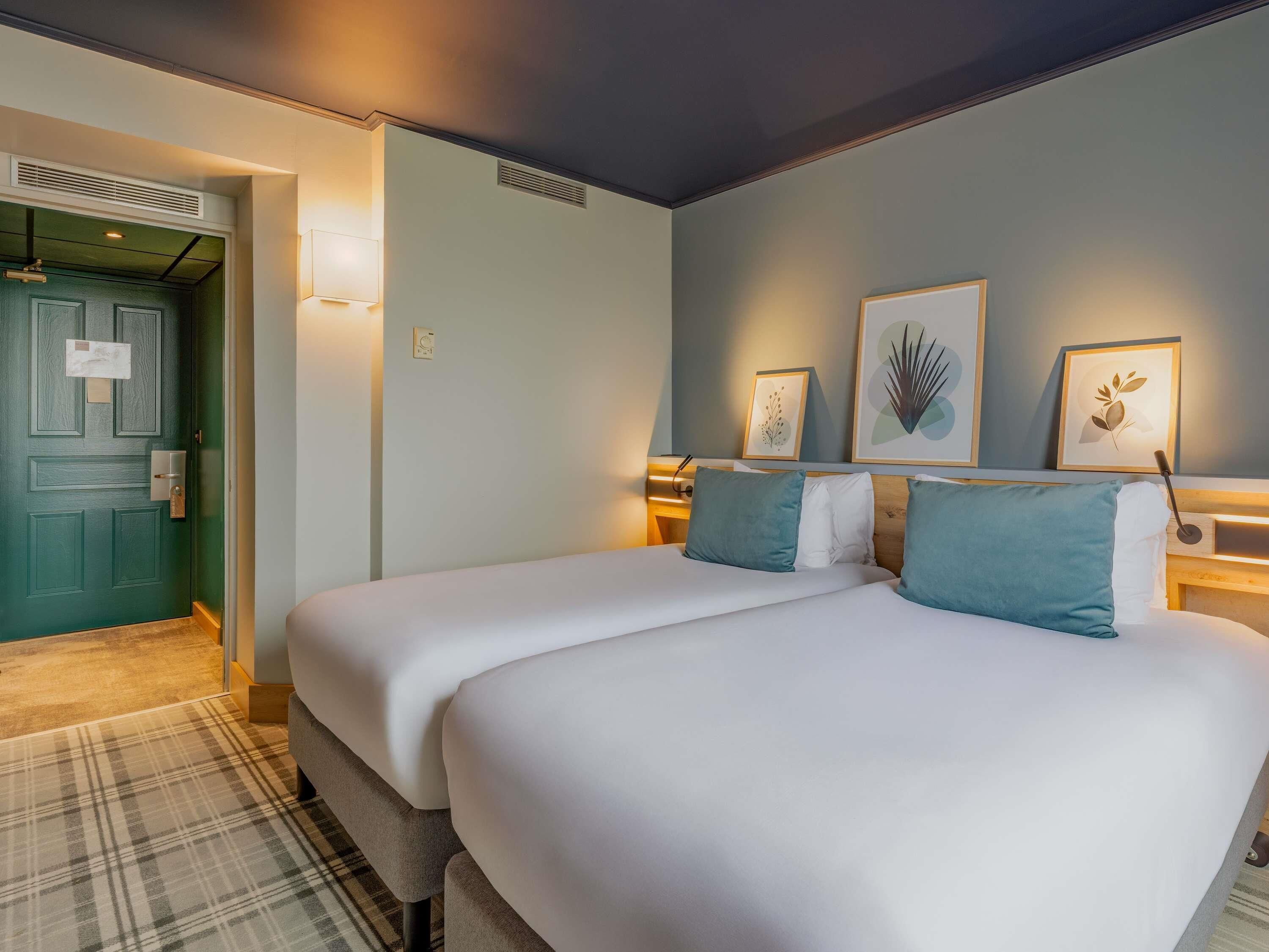 A hotel room with two beds, a green door, and wall-mounted artwork.