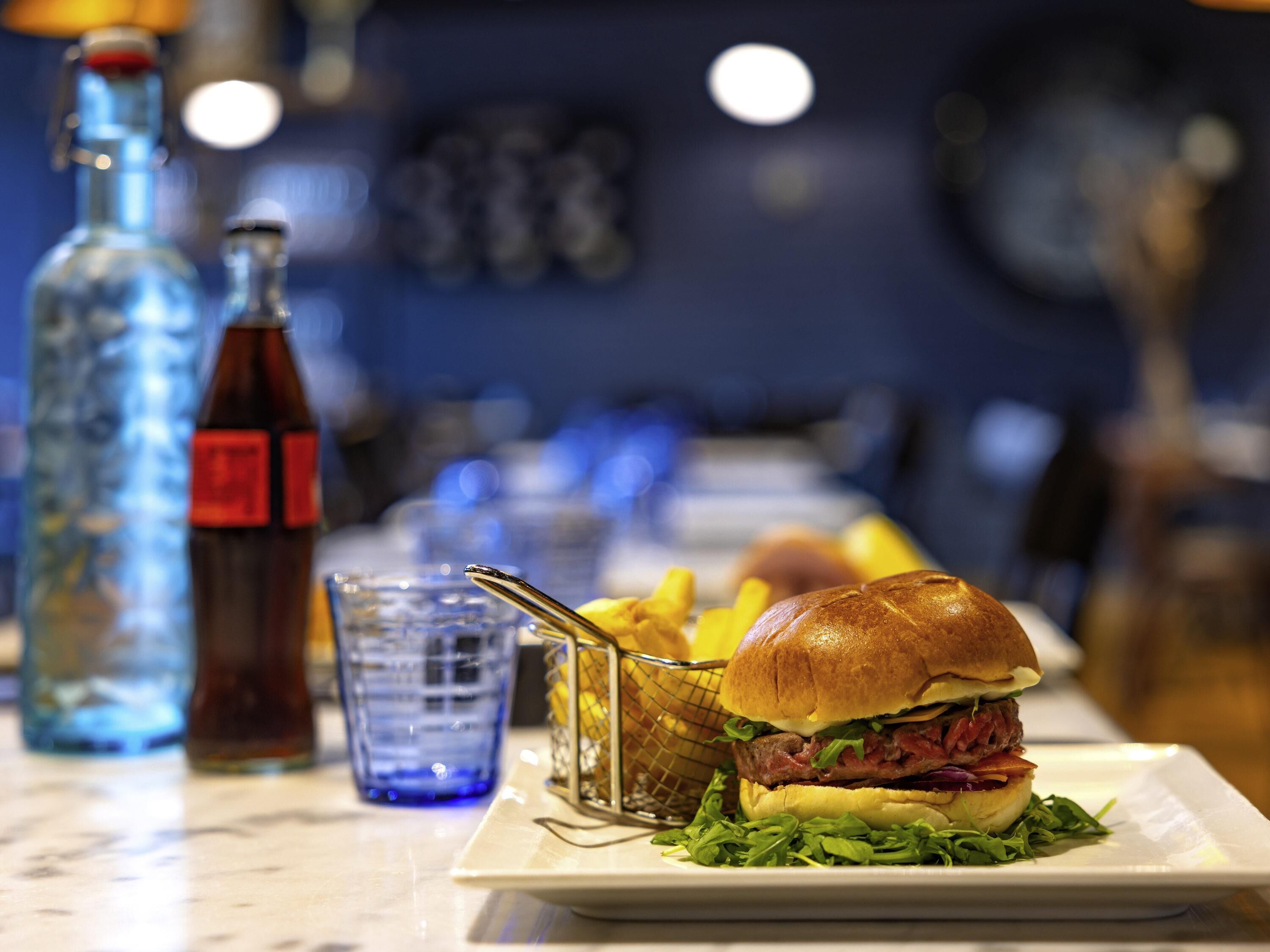 Una hamburguesa con papas fritas y una bebida sobre una mesa.
