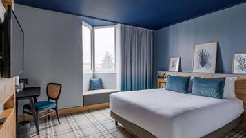 Une chambre d’hôtel avec un lit, un bureau, une chaise et une fenêtre avec des rideaux.