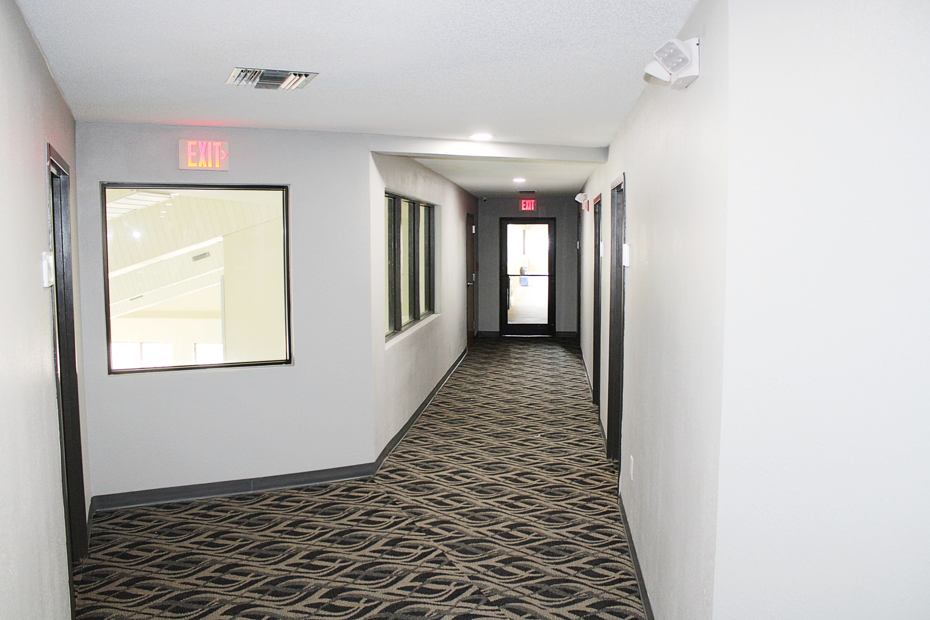 A hallway with patterned carpet, exit signs, and doors leading to other areas.