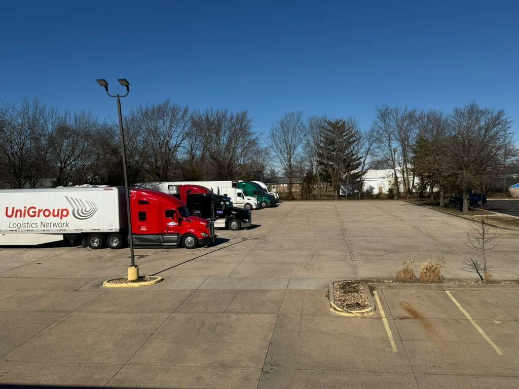 Ein Parkplatz mit mehreren Lastwagen, darunter ein roter Lastwagen mit dem Branding von UniGroup Logistics Network.