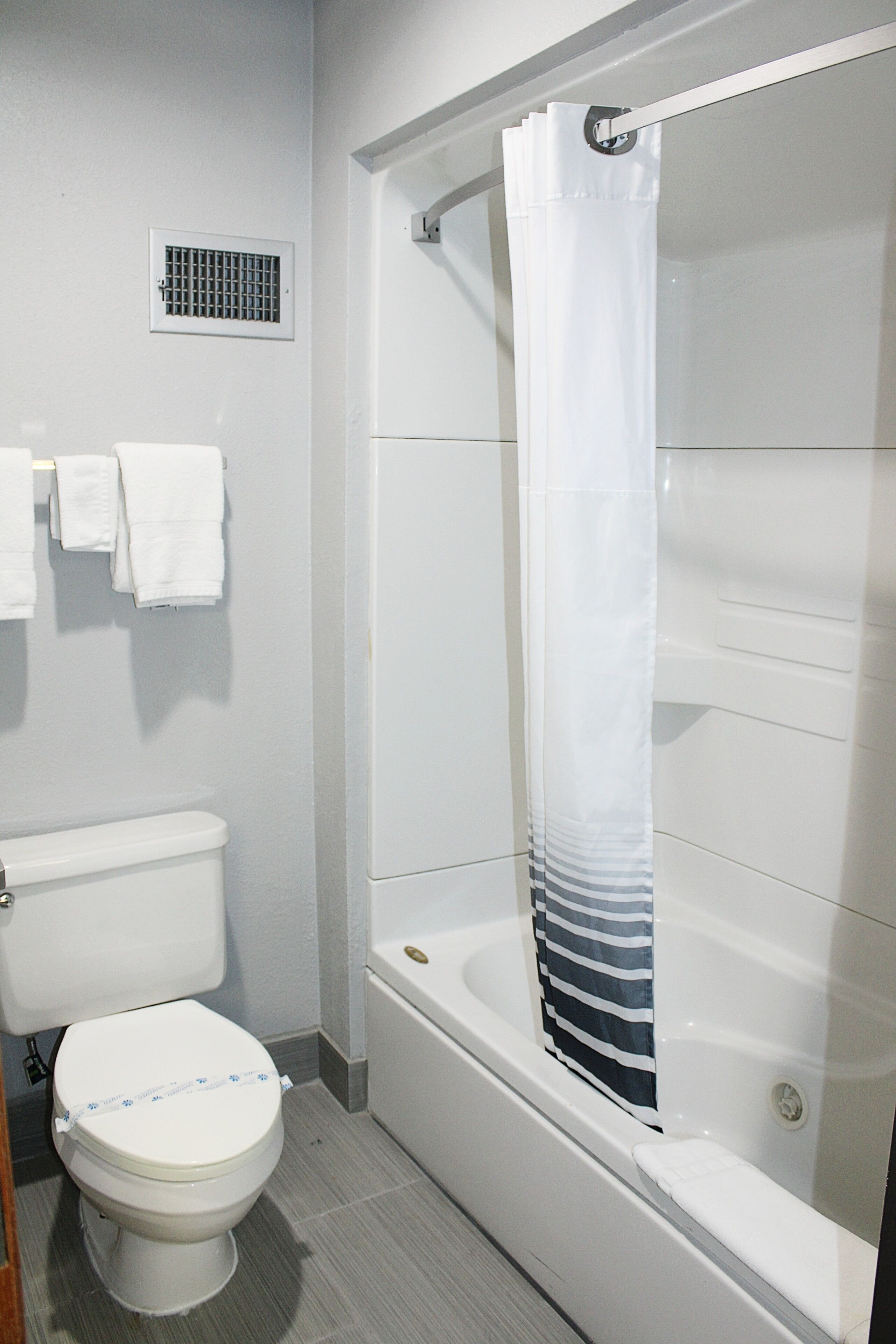 Un baño con inodoro, ducha con cortina blanca y toallero con toallas blancas.