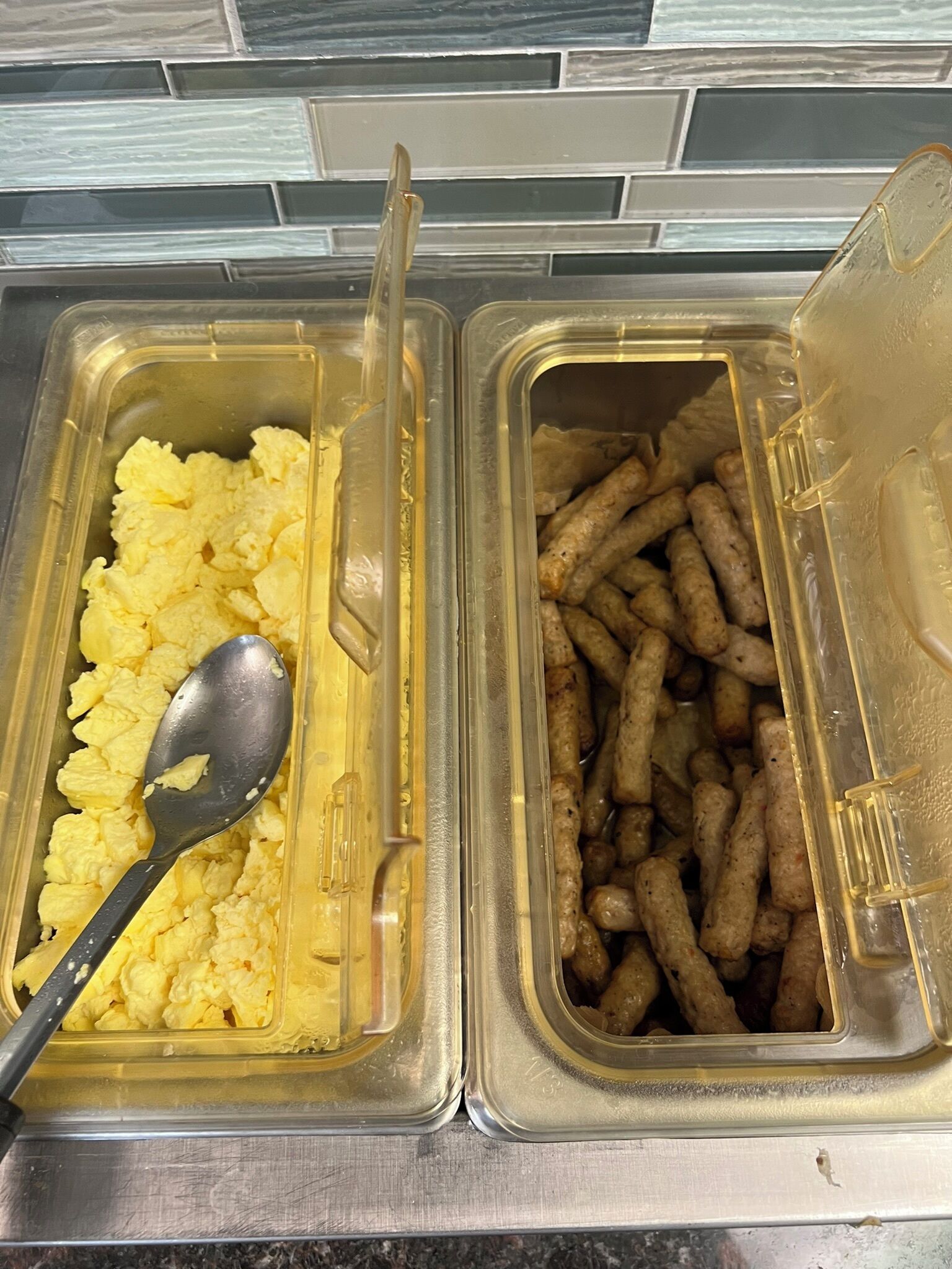 Two food dispensers with scrambled eggs and sausages.