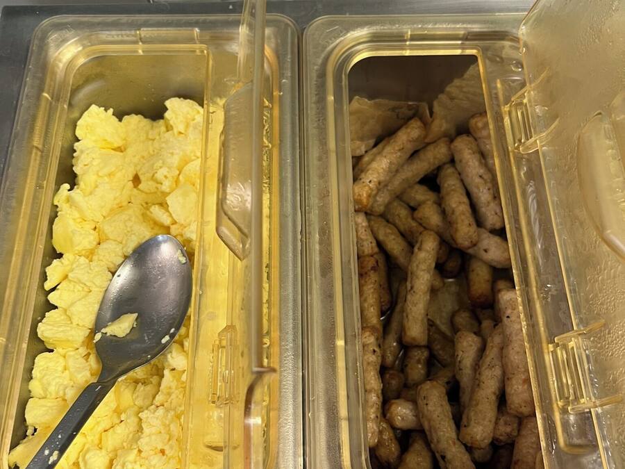 Two food dispensers with scrambled eggs and sausages.