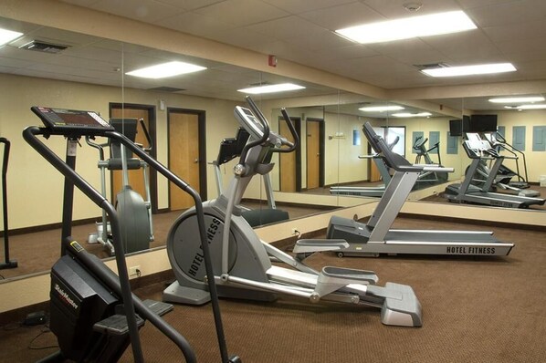 Un gimnasio de hotel con varias cintas de correr, elípticas y una bicicleta estática.
