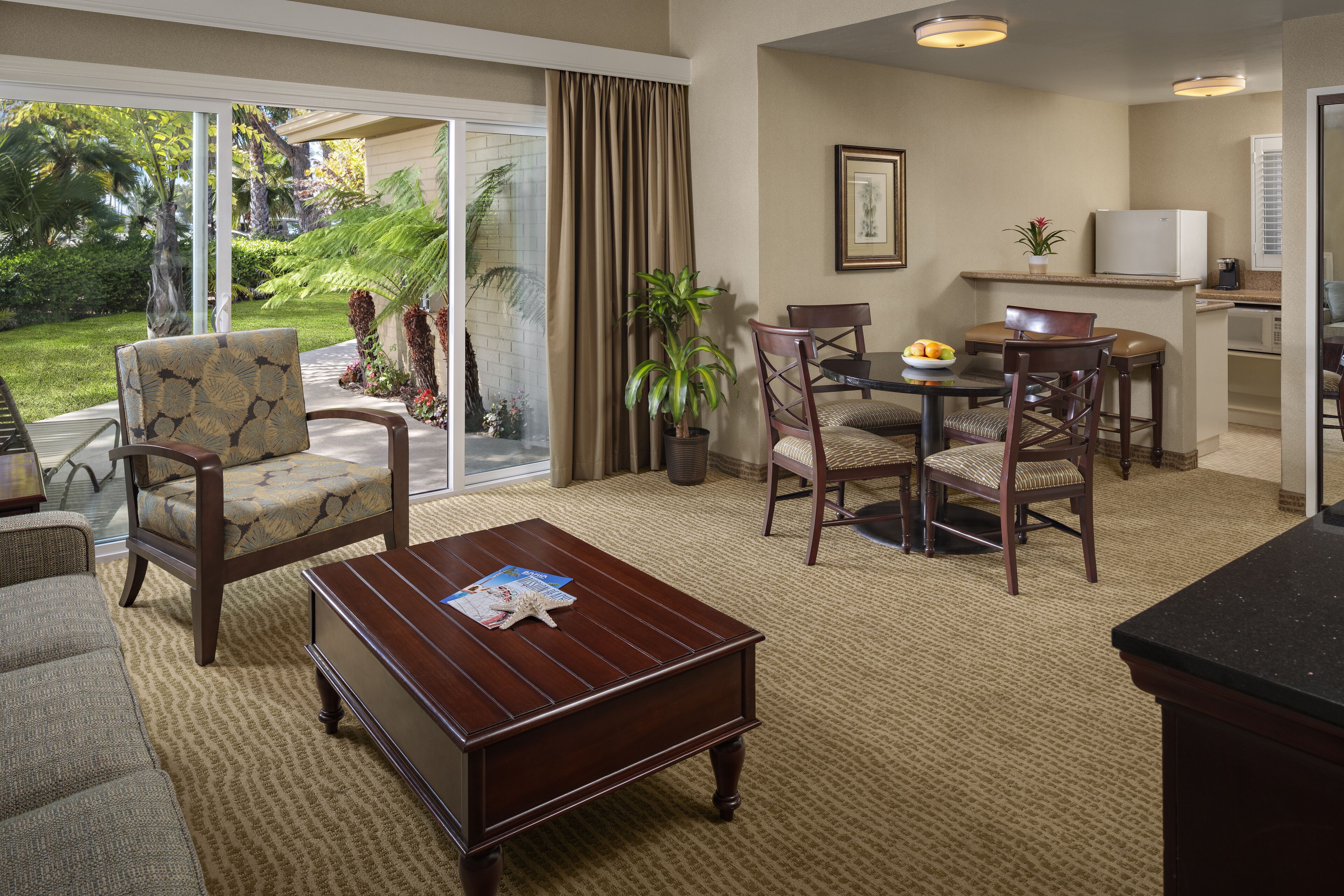 Une chambre d’hôtel comprenant un coin salon, une table à manger avec des chaises, une table basse et un coin cuisine équipé d’un réfrigérateur et d’un four à micro-ondes.