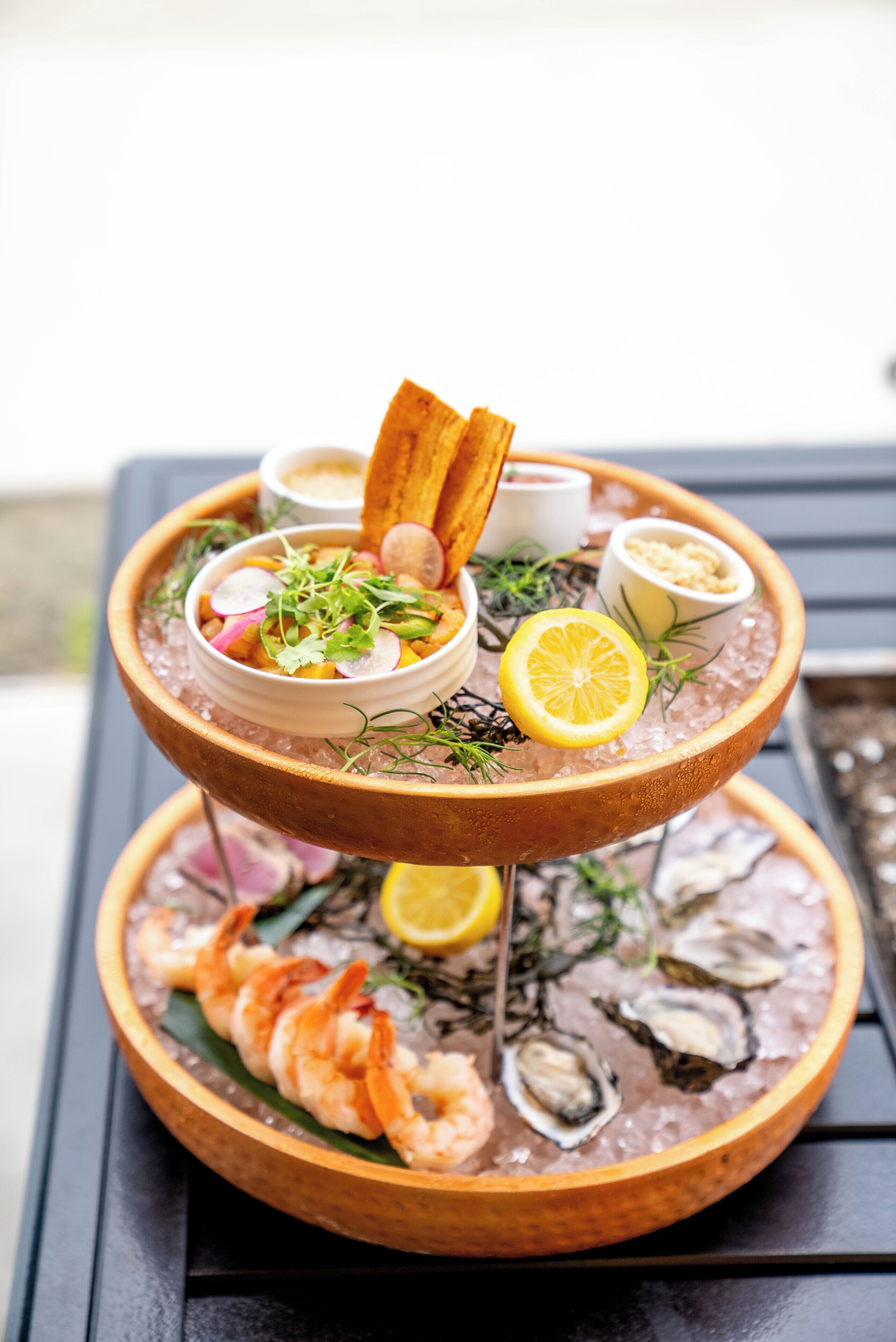 Una bandeja de mariscos con camarones, ostras y una ensalada sobre un soporte de madera.