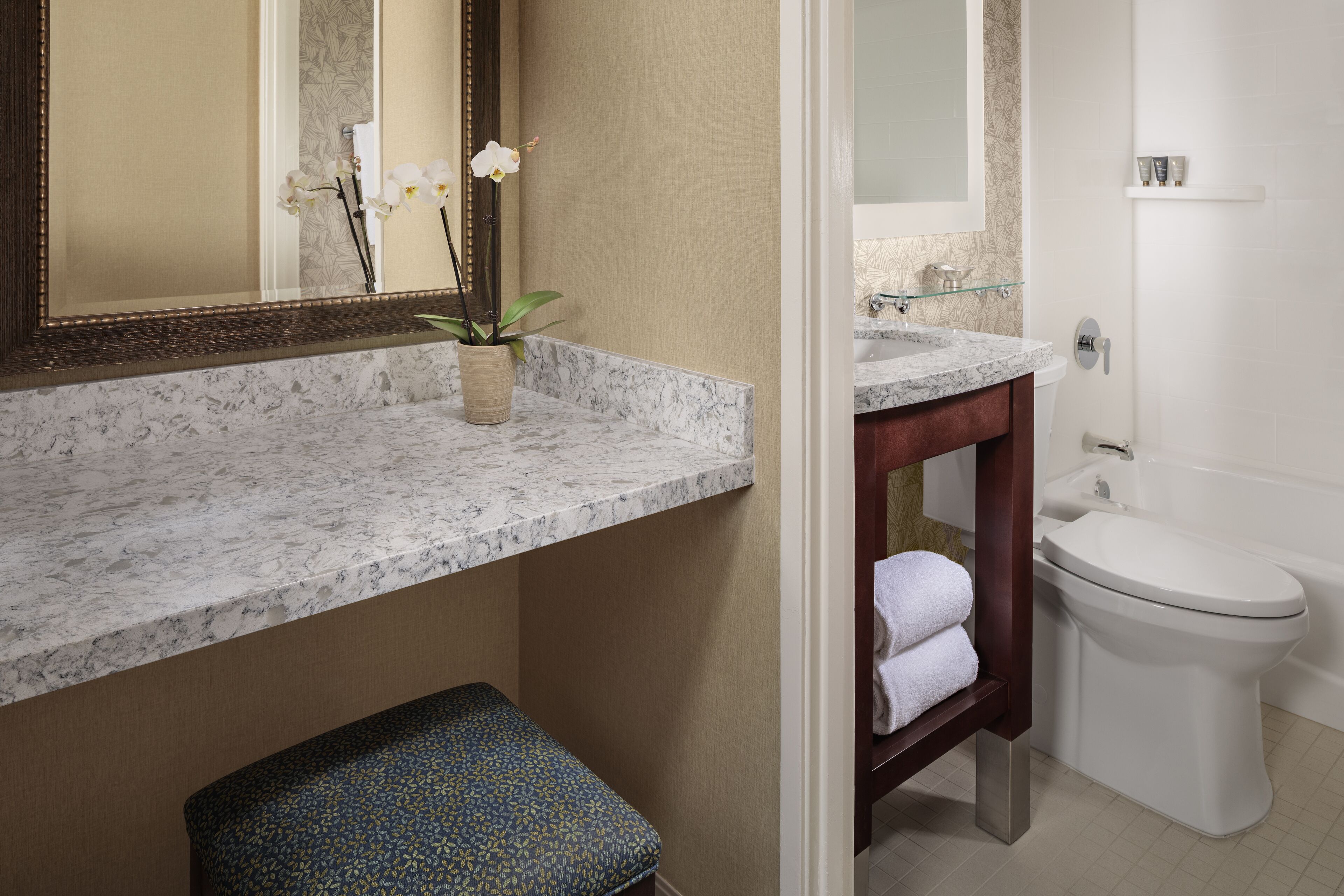 A bathroom with a marble countertop, a sink, a toilet, and a bench.