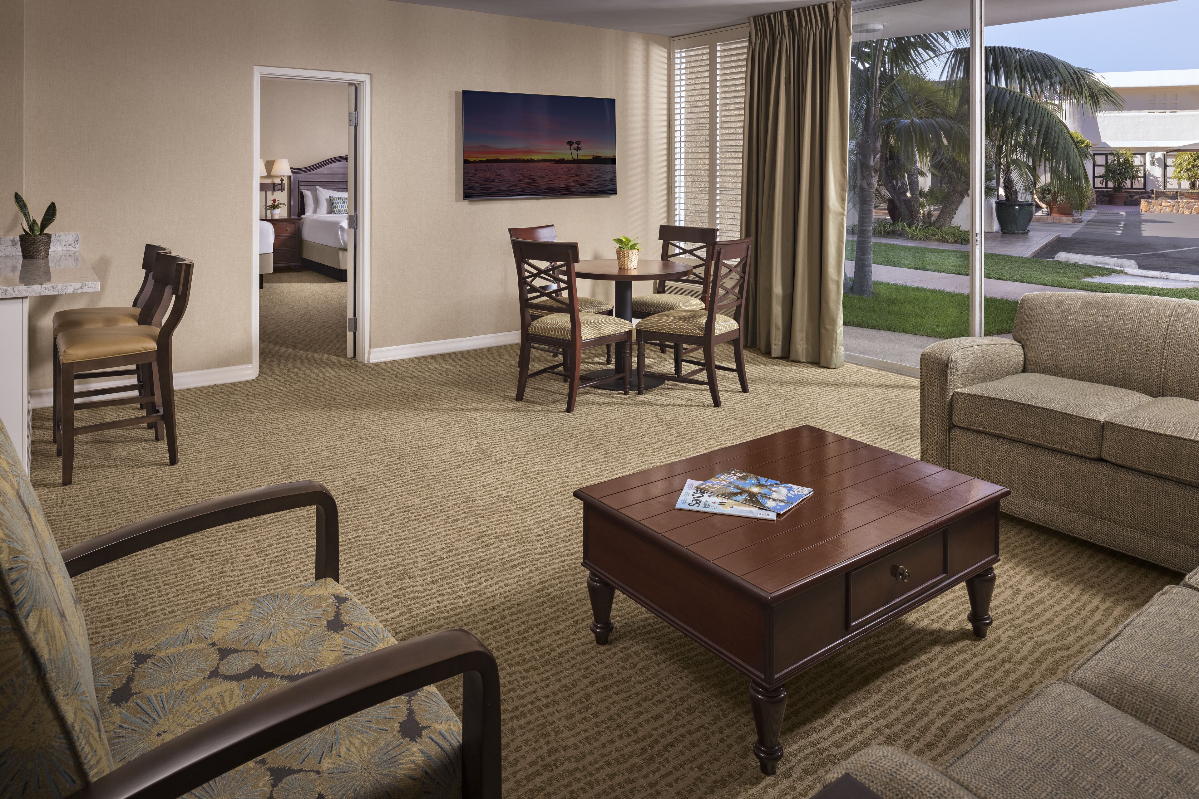 A hotel room with a dining area, a sofa, a coffee table, and a view of the outdoors.