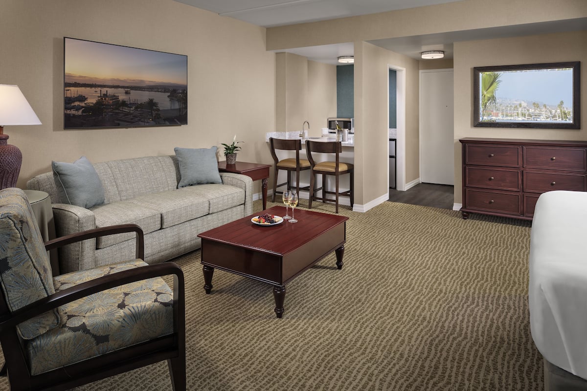 Une chambre d’hôtel équipée d’un canapé, d’un fauteuil, d’une table à manger et de chaises. Un téléviseur est fixé au mur et une fenêtre offre une vue agréable.
