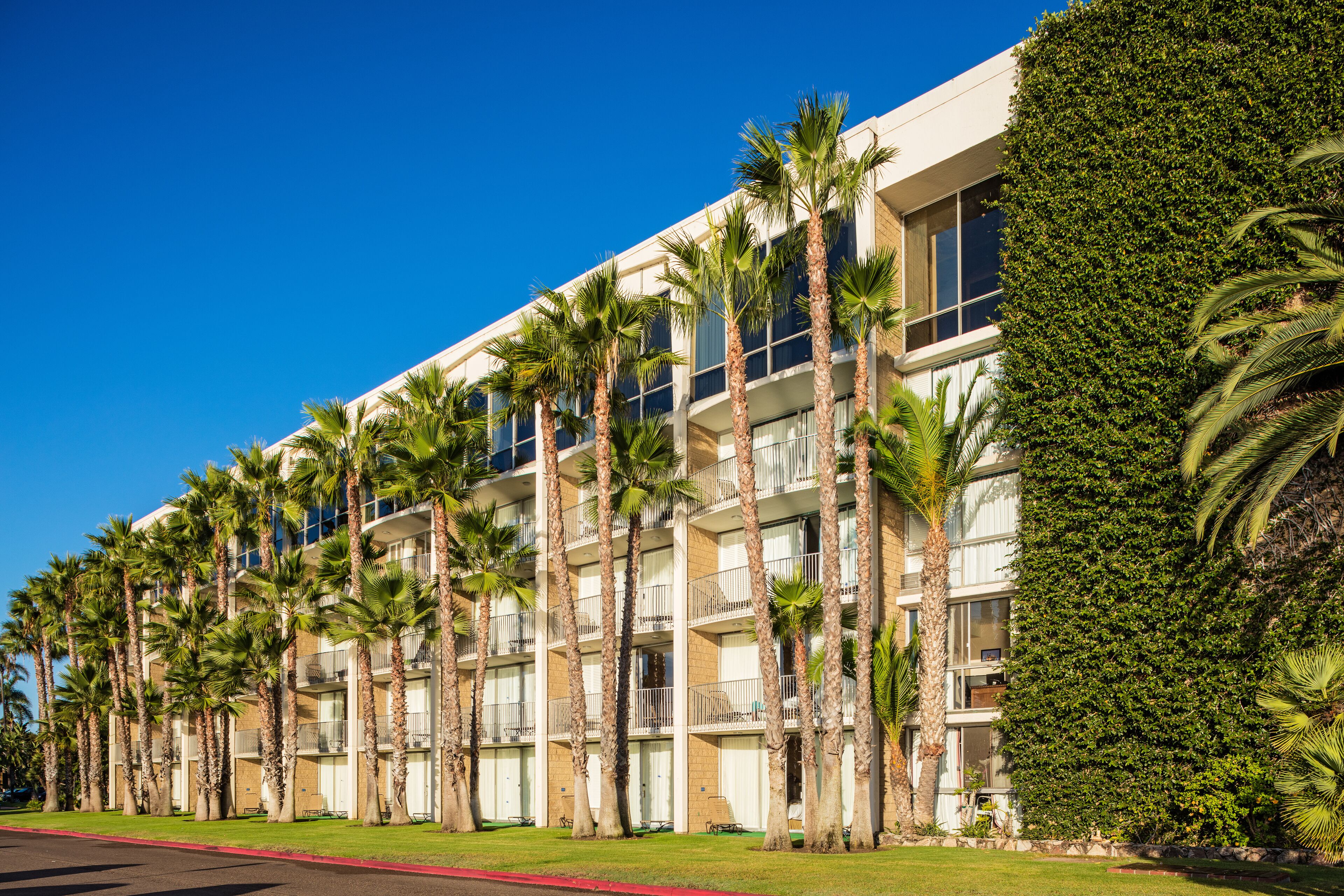 A multi-story hotel with balconies, palm trees, and a well-maintained lawn.