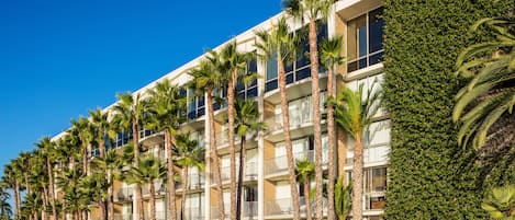 A multi-story hotel with balconies, palm trees, and a well-maintained lawn.