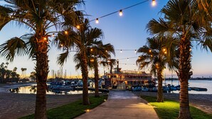A waterfront property with a pathway lined by palm trees and string lights, leading to a building with a dock and boats. - Bahia Resort Hotel (San Diego)