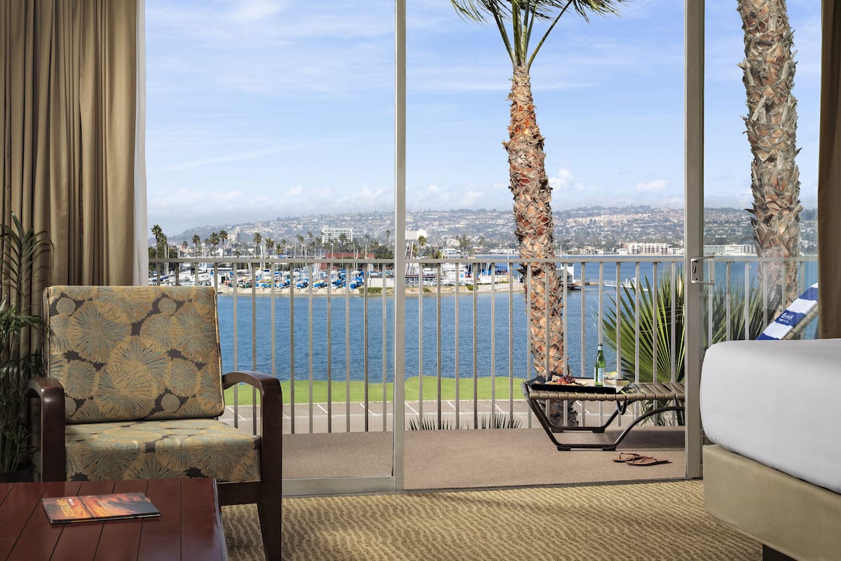 Une chambre d’hôtel avec vue sur le port de plaisance, un balcon avec un canapé et une table, et un palmier.