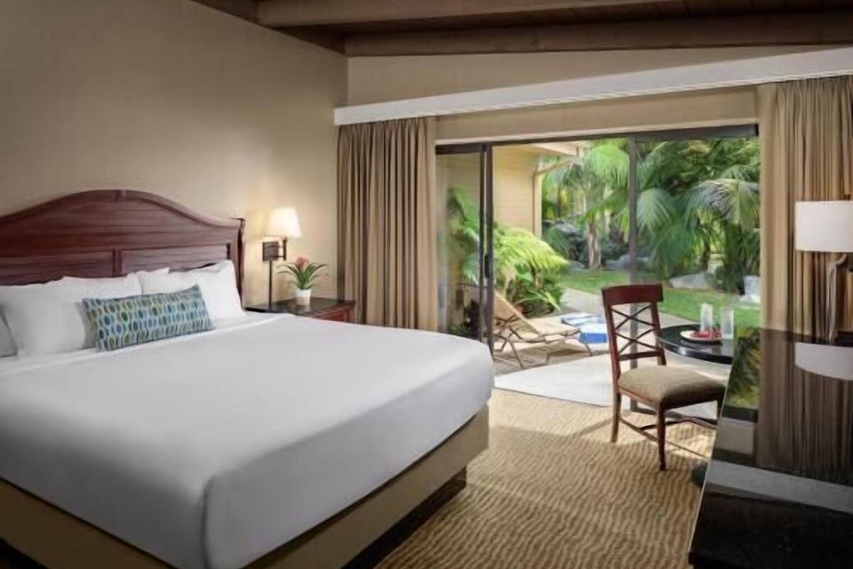 Une chambre d’hôtel équipée d’un lit, d’un bureau, d’une chaise et offrant une vue sur un jardin grâce à une porte vitrée.
