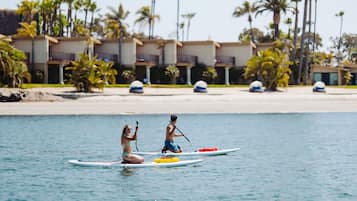 Two people paddleboarding on a calm sea with a resort in the background.