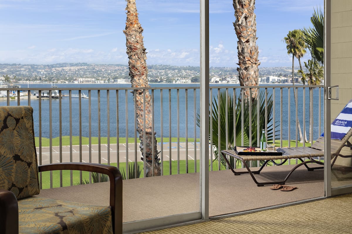 Un balcon donnant sur une étendue d’eau, avec des palmiers et une chaise.