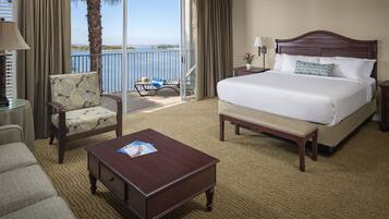 A hotel room with a large bed, a chair, a coffee table, and a view of the water.