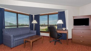 A hotel room with a sofa, desk, chair, TV, and large windows with curtains. - Days Inn by Wyndham Sidney NE (Sidney)