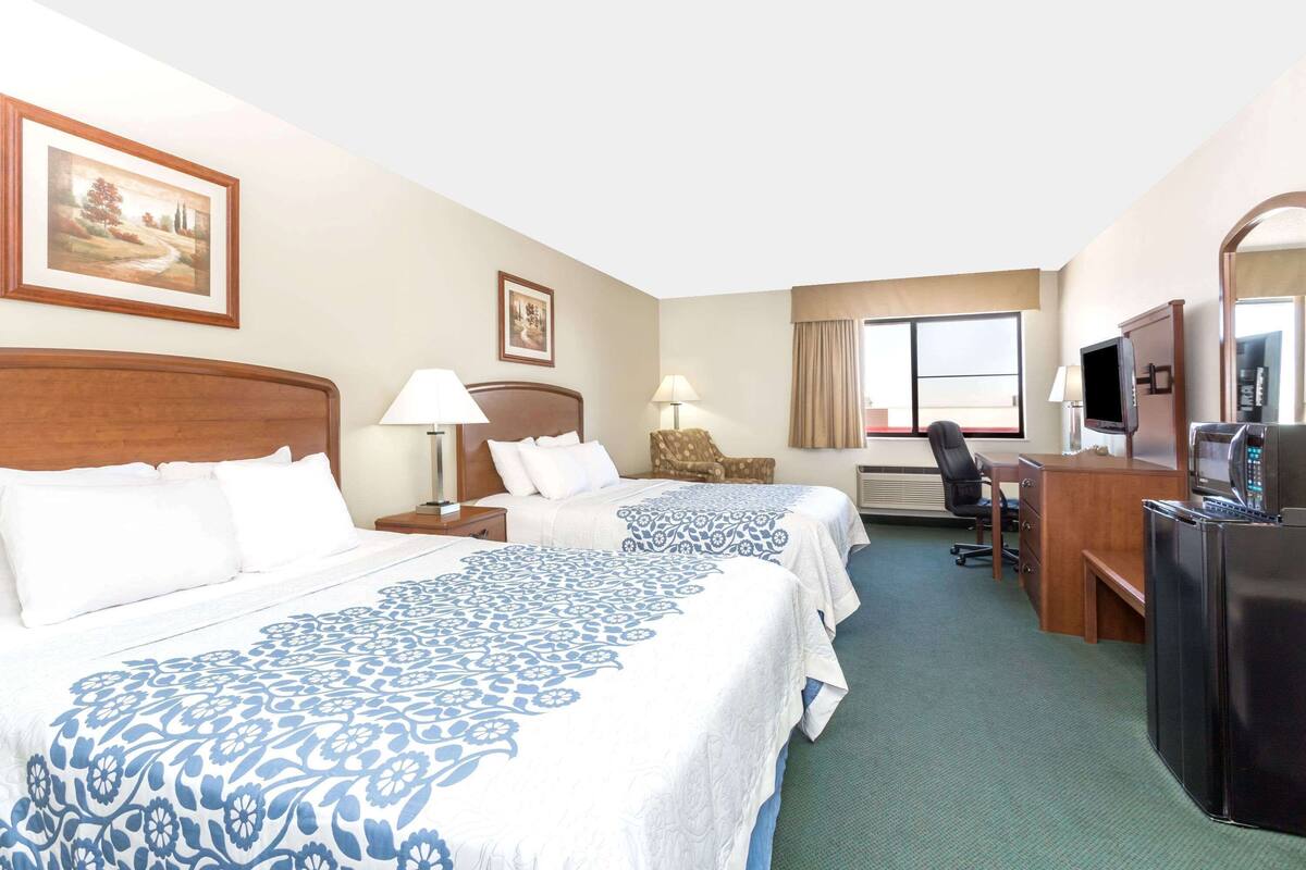 A hotel room with two beds, a desk, a chair, a television, and a refrigerator.