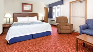 A hotel room with a large bed, two bedside tables with lamps, a brown armchair, a blue armchair, and a wooden table. - Days Inn by Wyndham Sidney NE (Sidney)