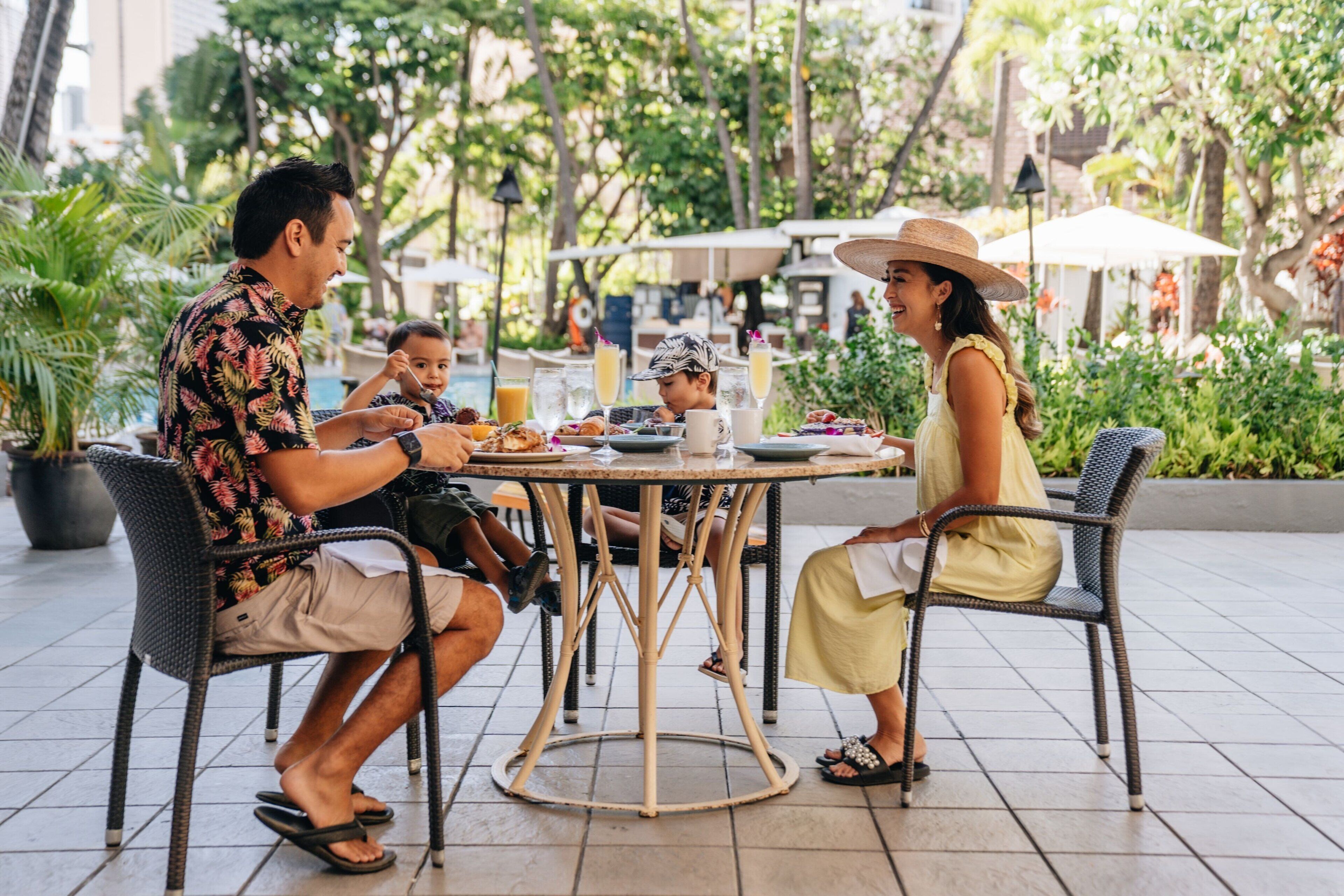 A family dining at an outdoor table with a view of a pool and greenery.