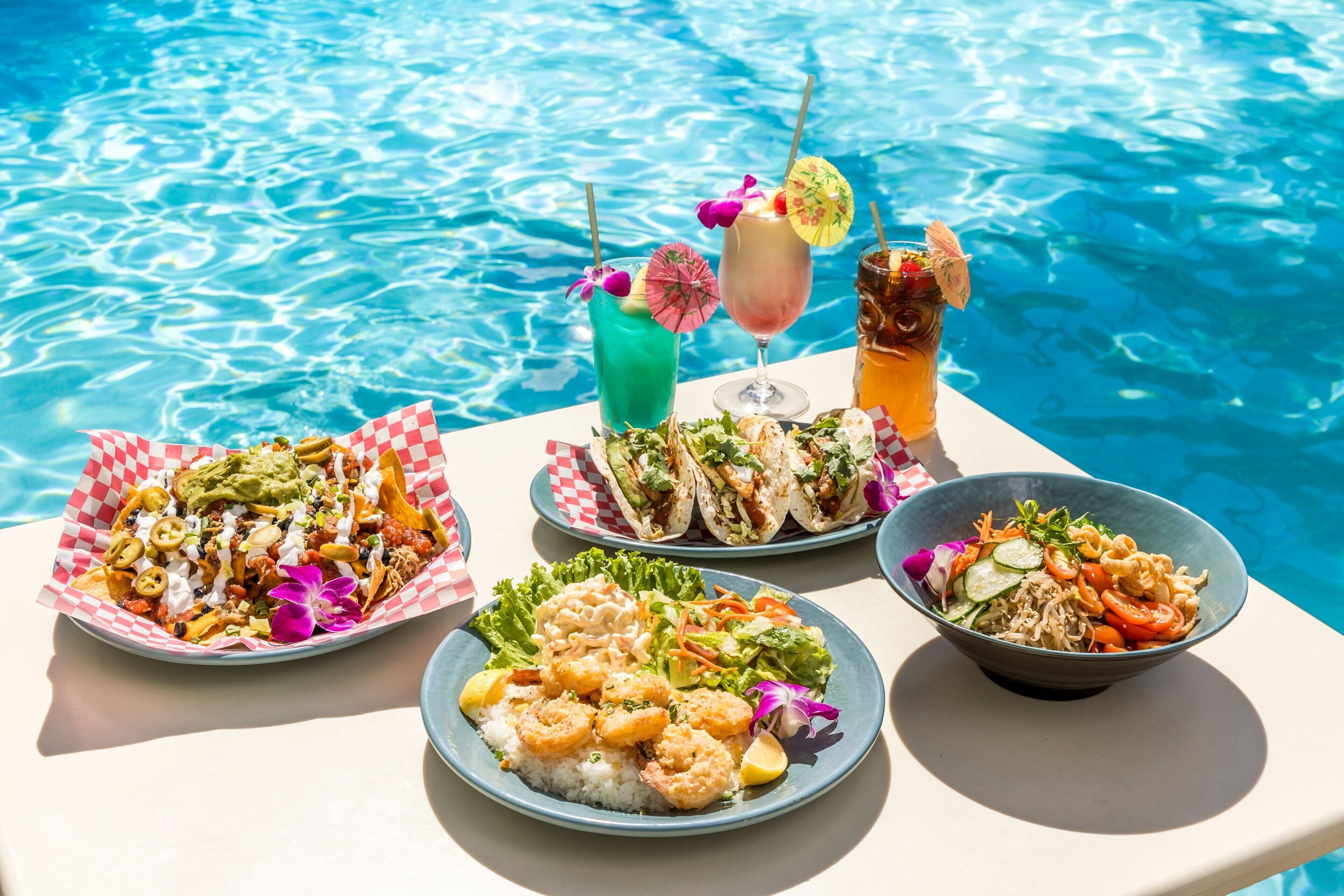 A table with various dishes and drinks by a pool.