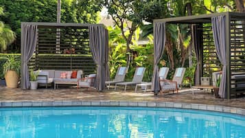 Zona de piscina con área de estar techada, sillas de descanso y un sofá.