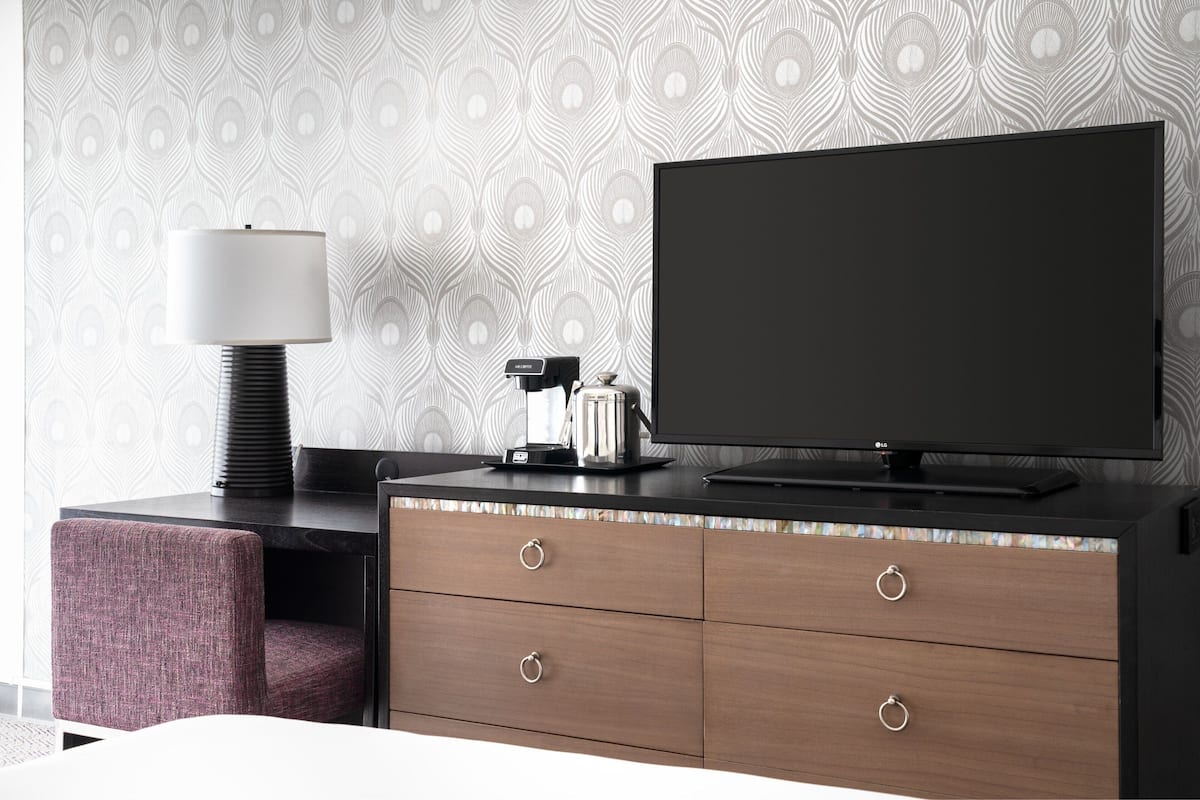 Una habitación de hotel moderna con una televisión de pantalla plana grande sobre un aparador de madera, una lámpara y una cafetera.