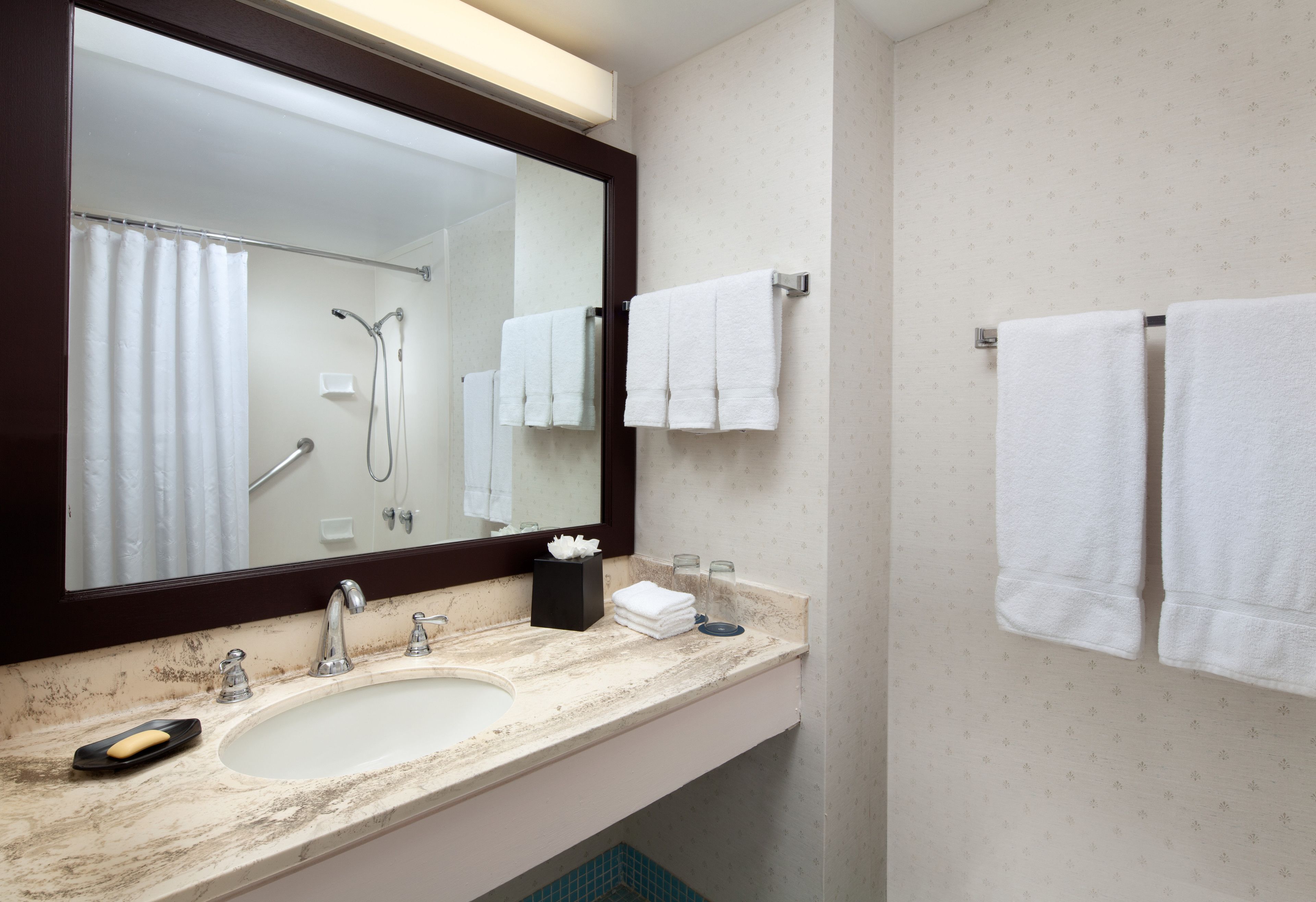 A bathroom with a large mirror, a sink, a shower, and two towels hanging on the wall.
