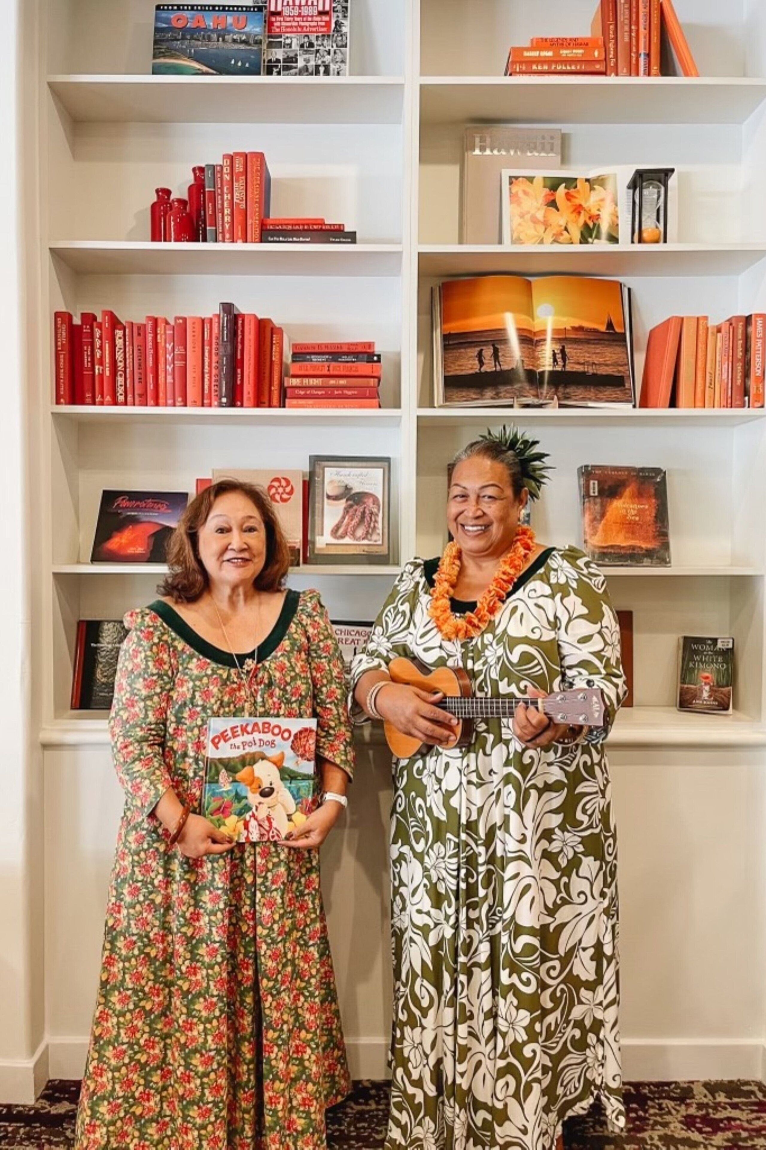Two people standing in front of a bookshelf filled with books and framed pictures.