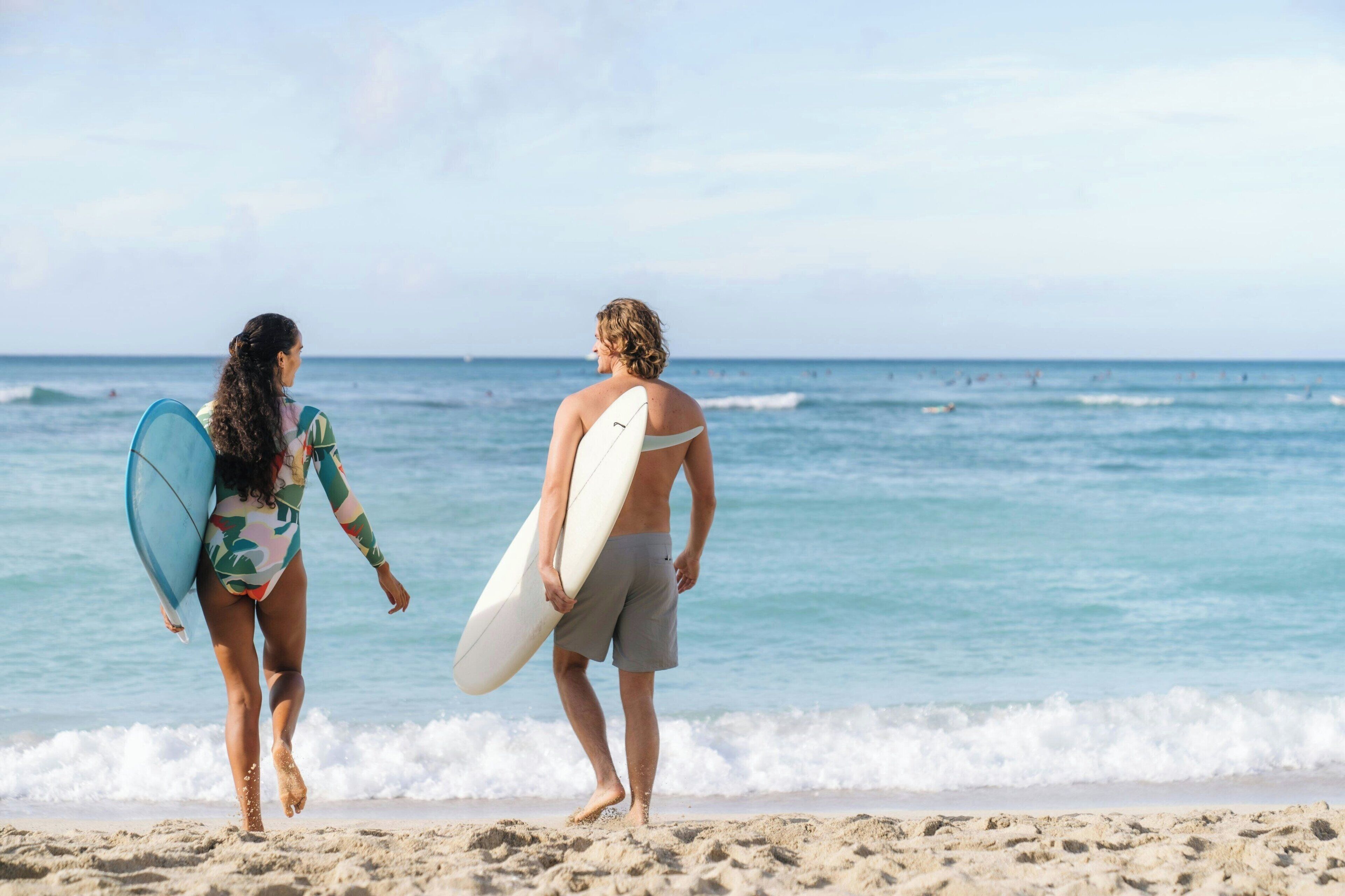 Two people walking on a beach with surfboards, heading towards the ocean.