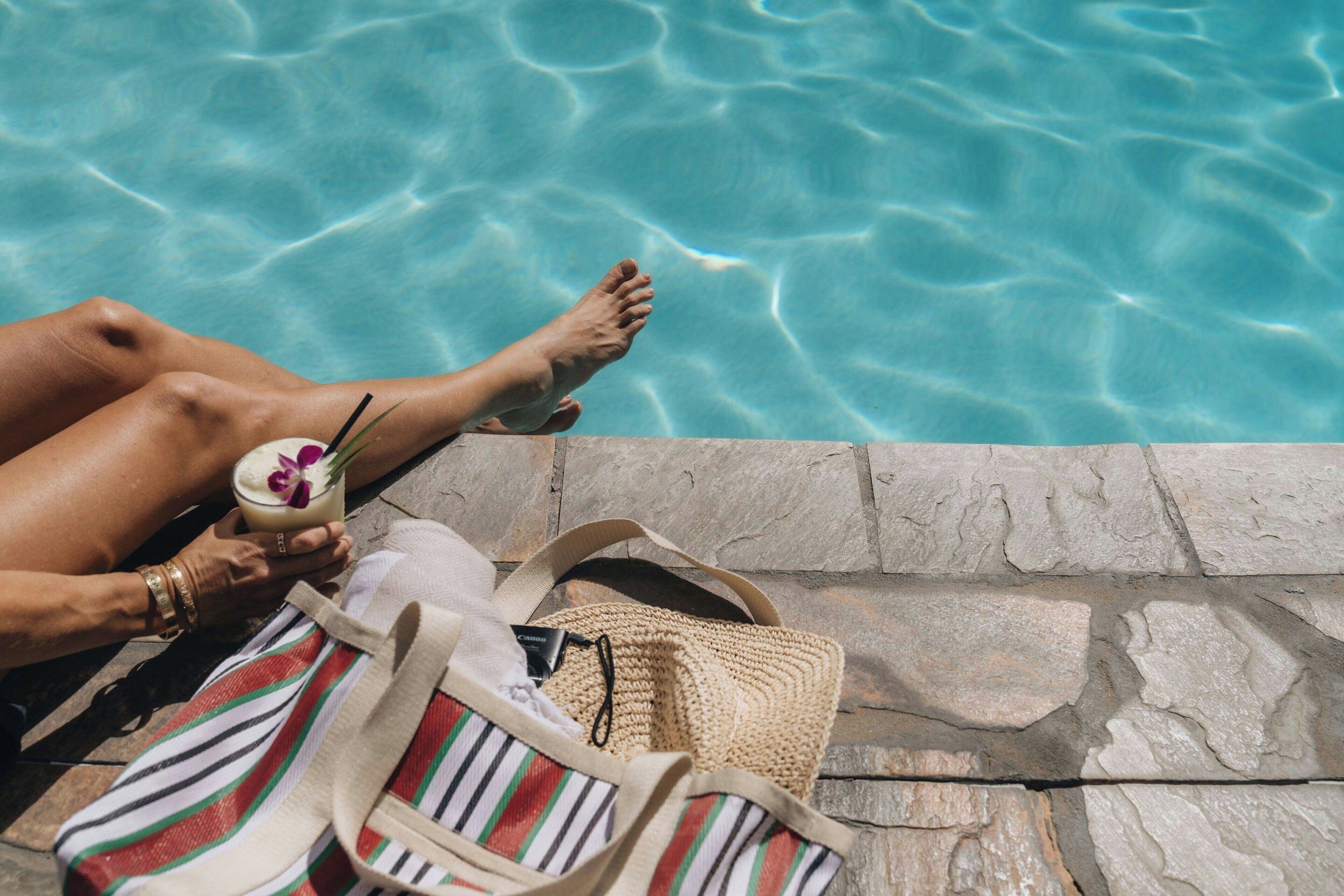 Vista de la piscina con borde de piedra, un bolso a rayas y una bebida con pajita.