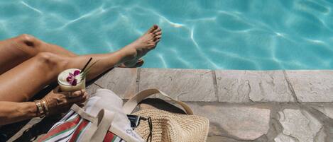 Vista de la piscina con borde de piedra, un bolso a rayas y una bebida con pajita.