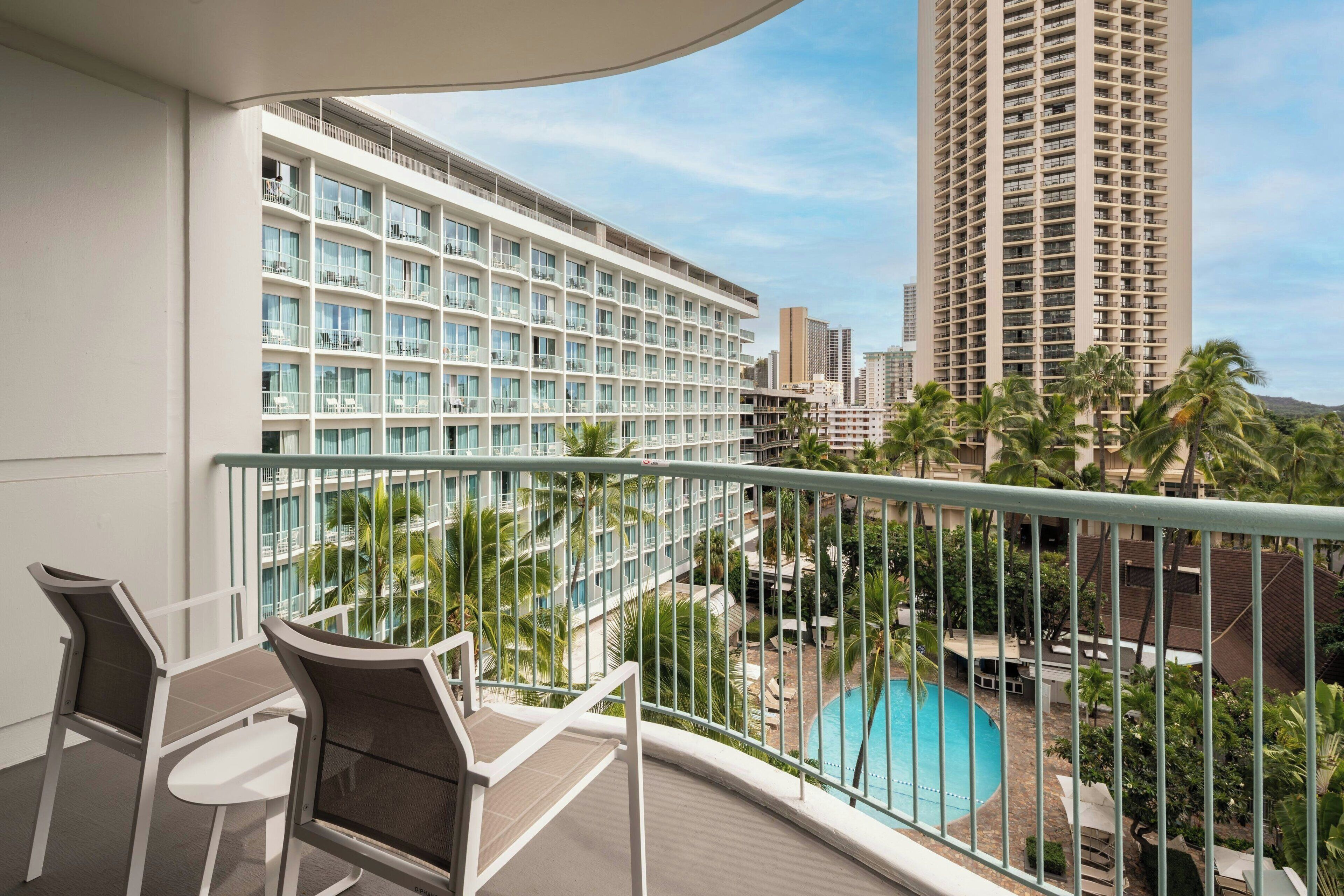 A balcony with a pool view, white-framed windows, and a view of a tall building.