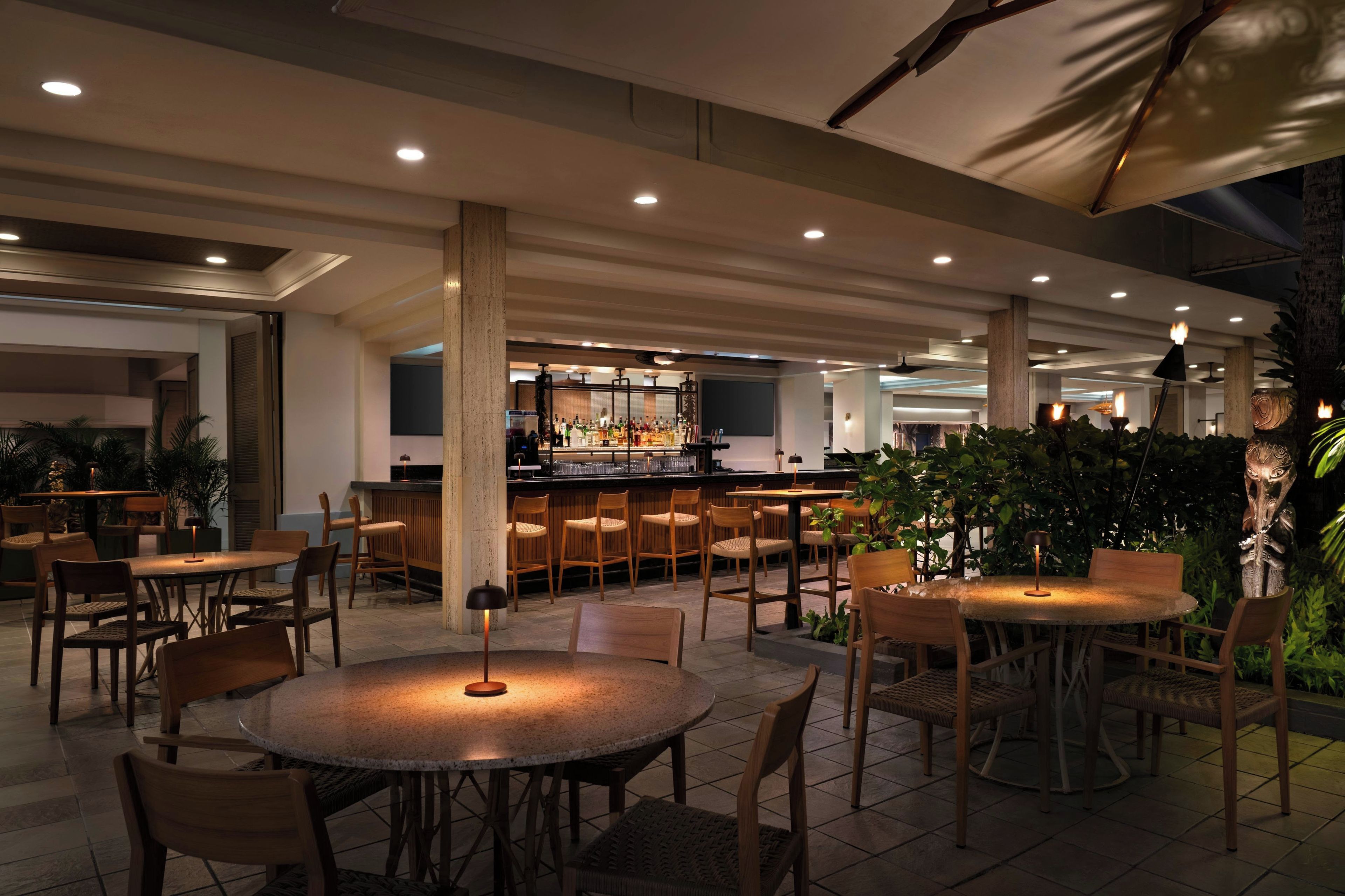 A restaurant with round tables and chairs, a bar area, and a ceiling with recessed lighting.